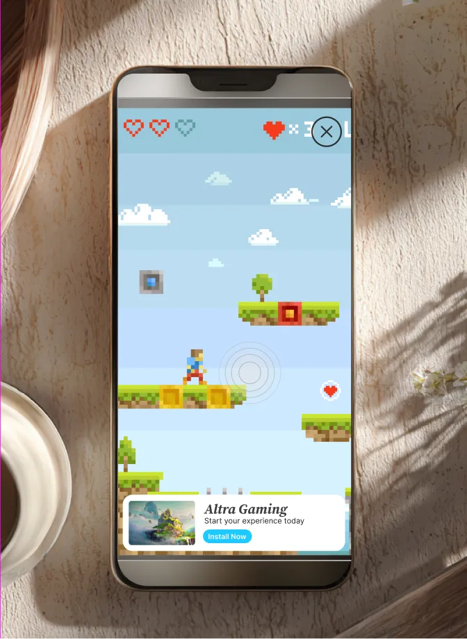 Mobile phone on a table showing a pixelated platform video game with a character and floating hearts.