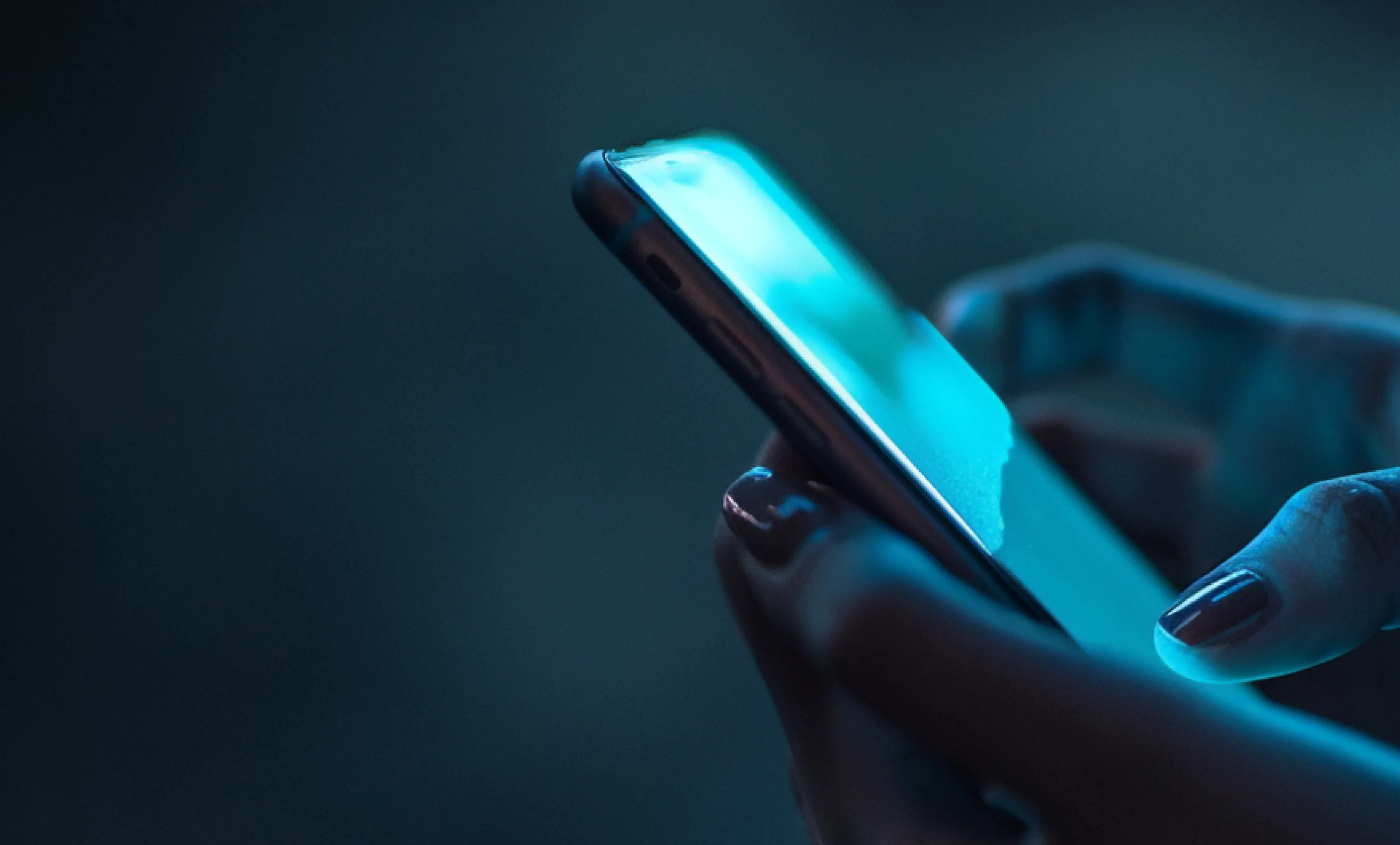 Close-up of hands holding and using a smartphone with blue screen light in a dark setting.