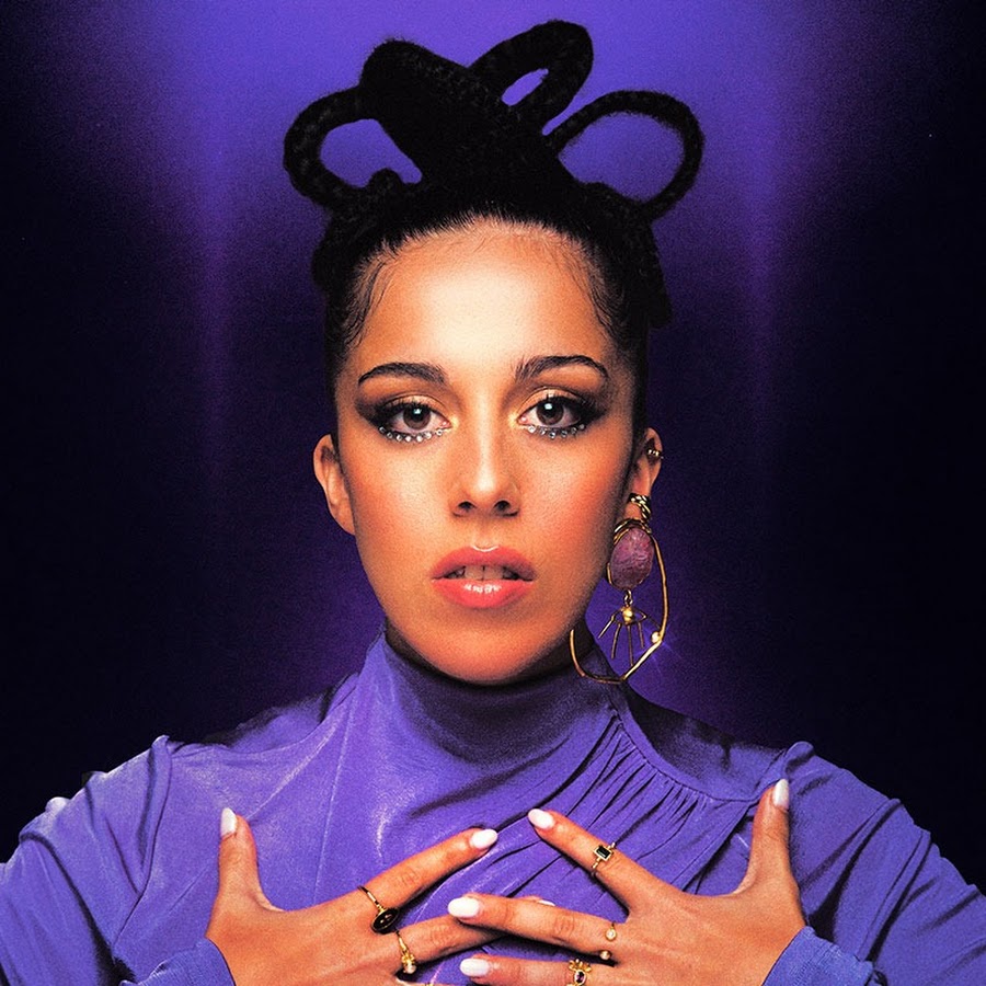 woman with hair tied in circles with a dark background and hands over her chest