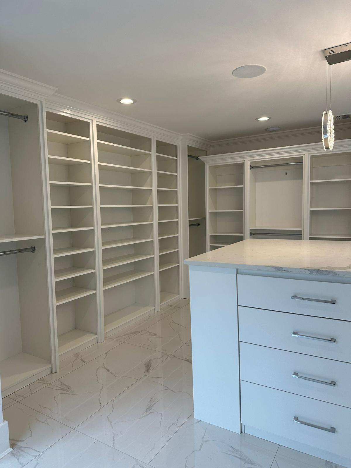 Spacious white custom walk-in closet with built-in shelves, hanging rods, and an island in a New Jersey home