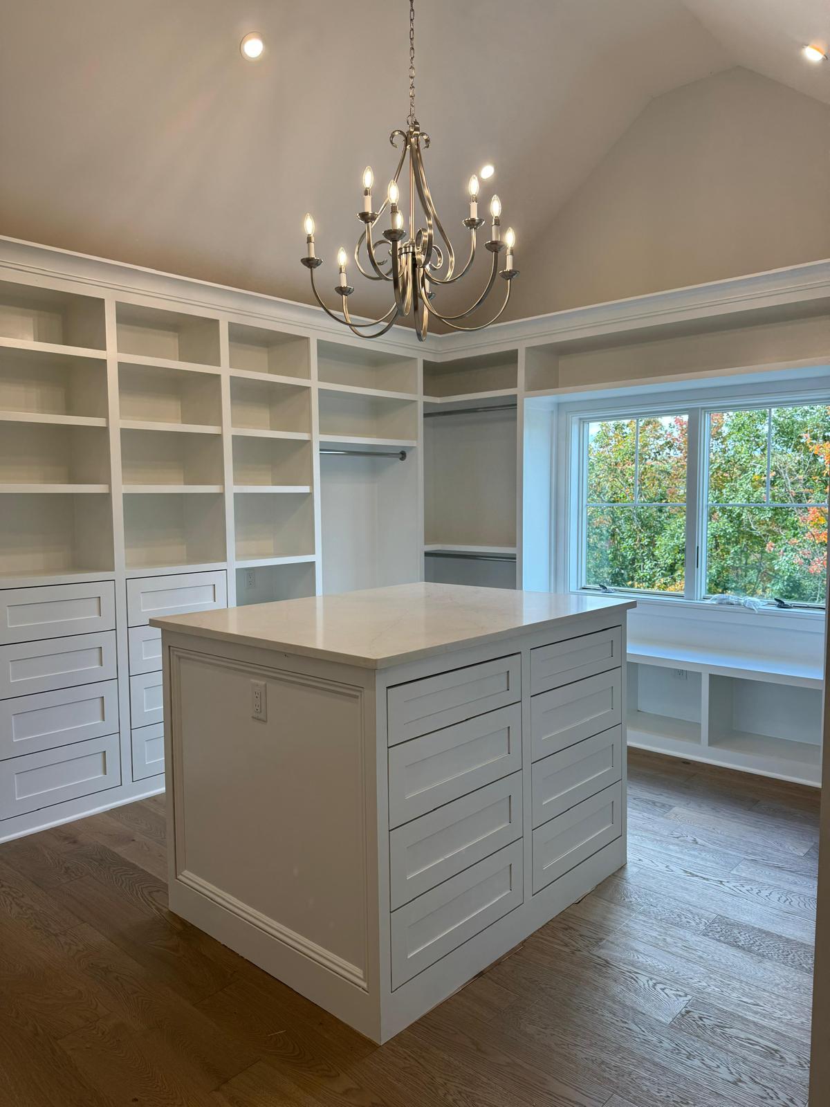 White custom walk-in closet with built-in shelving, drawers, island, and window seat in a New Jersey home
