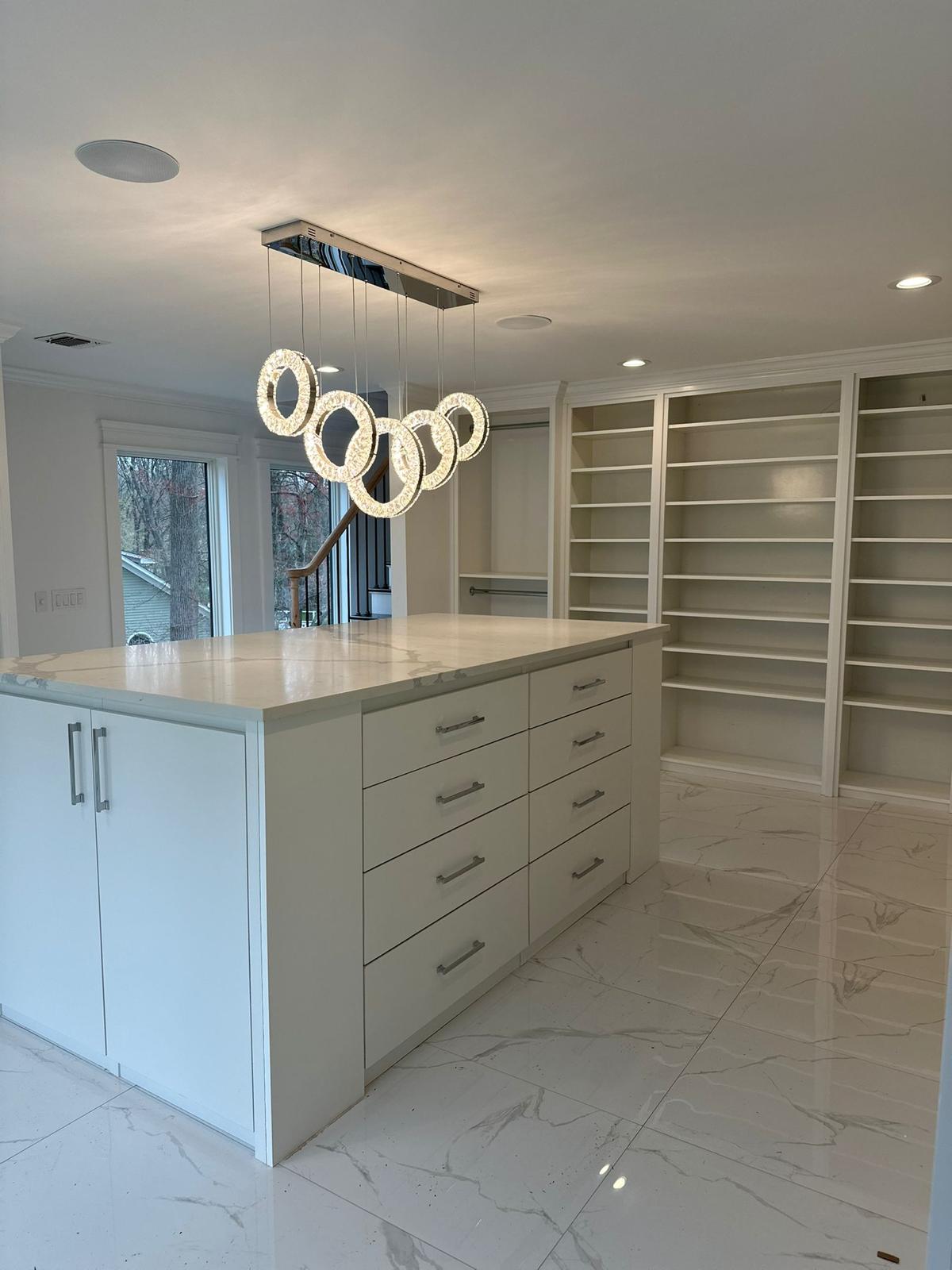 Spacious custom walk-in closet featuring white built-in cabinetry, open shelves, and a large center island with drawers in NJ.