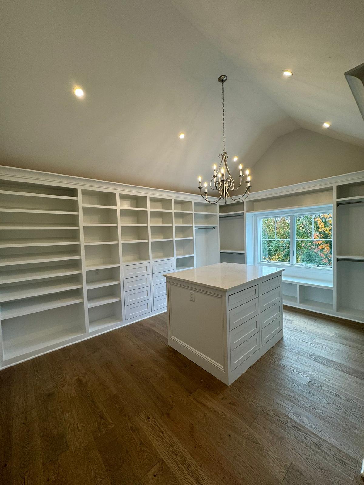 Spacious custom walk-in closet in a New Jersey home with white built-in cabinetry, shelves, drawers, and an island