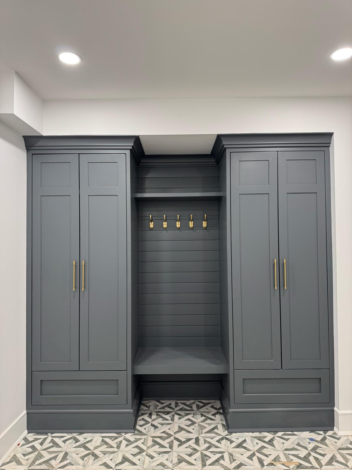 Custom built-in mudroom unit with dark gray cabinets, bench, shiplap paneling, and brass coat hooks in a NJ home