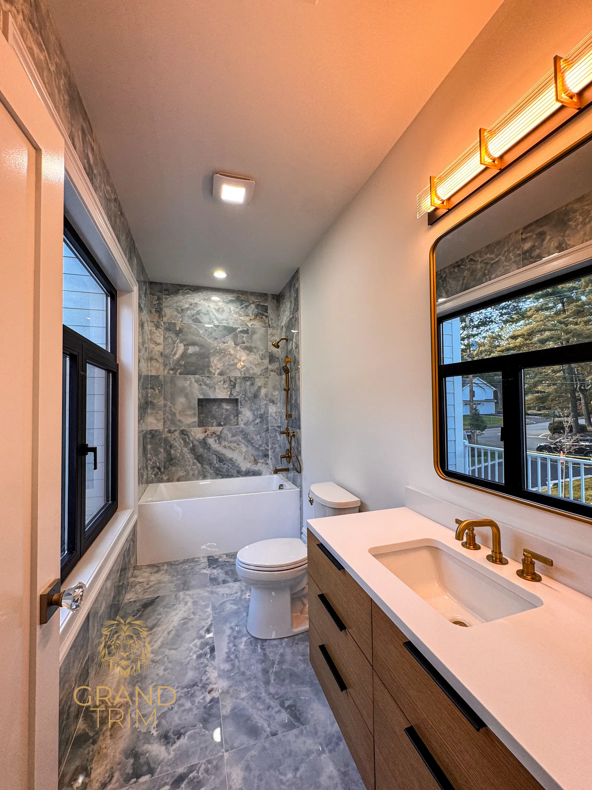 White window and door casing in a modern bathroom with wood vanity and gray marble tiles in New Jersey