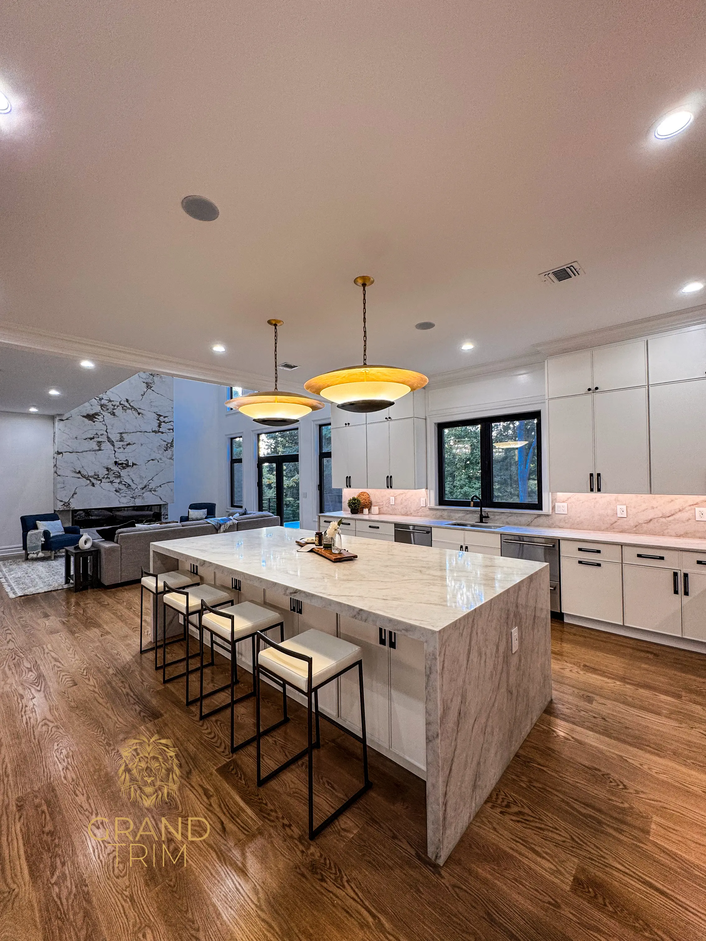 Modern white kitchen cabinetry with a large marble island and a striking marble fireplace in an open-concept NJ home
