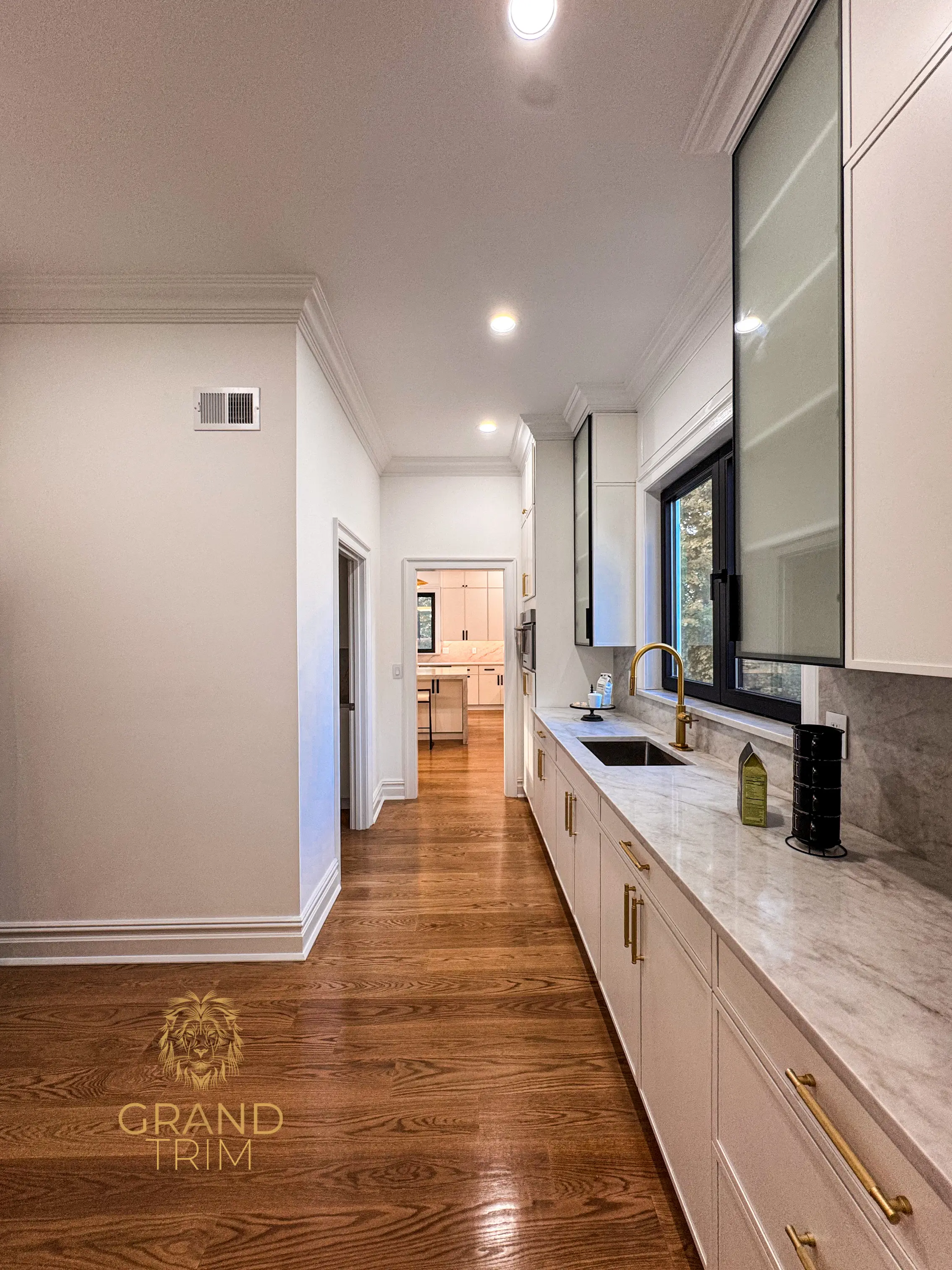 White kitchen cabinetry with marble countertops and gold fixtures in a New Jersey home, featuring decorative crown molding in the adjacent hallway.