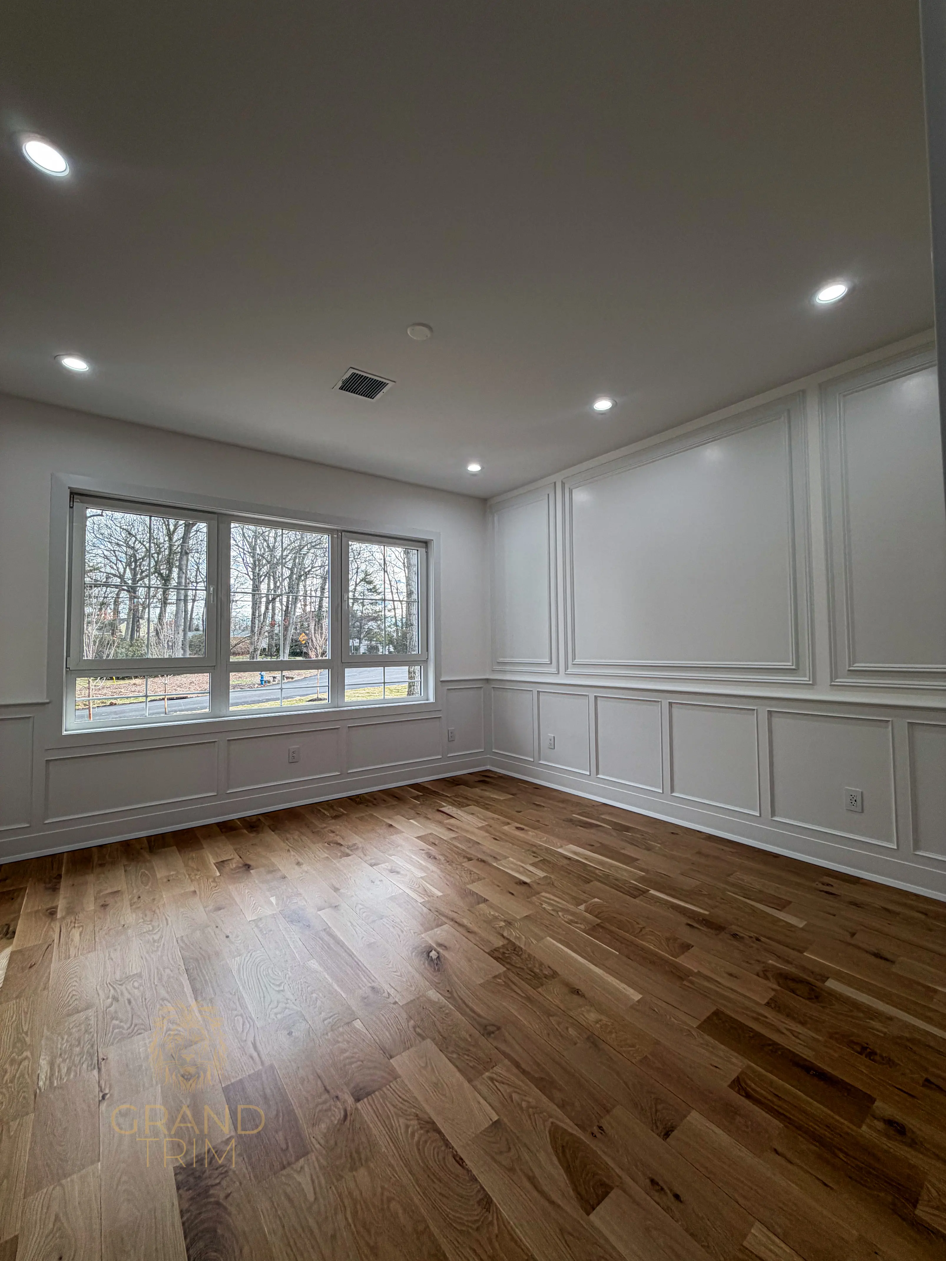 White decorative wall paneling with applied molding in a modern room with large windows in New Jersey