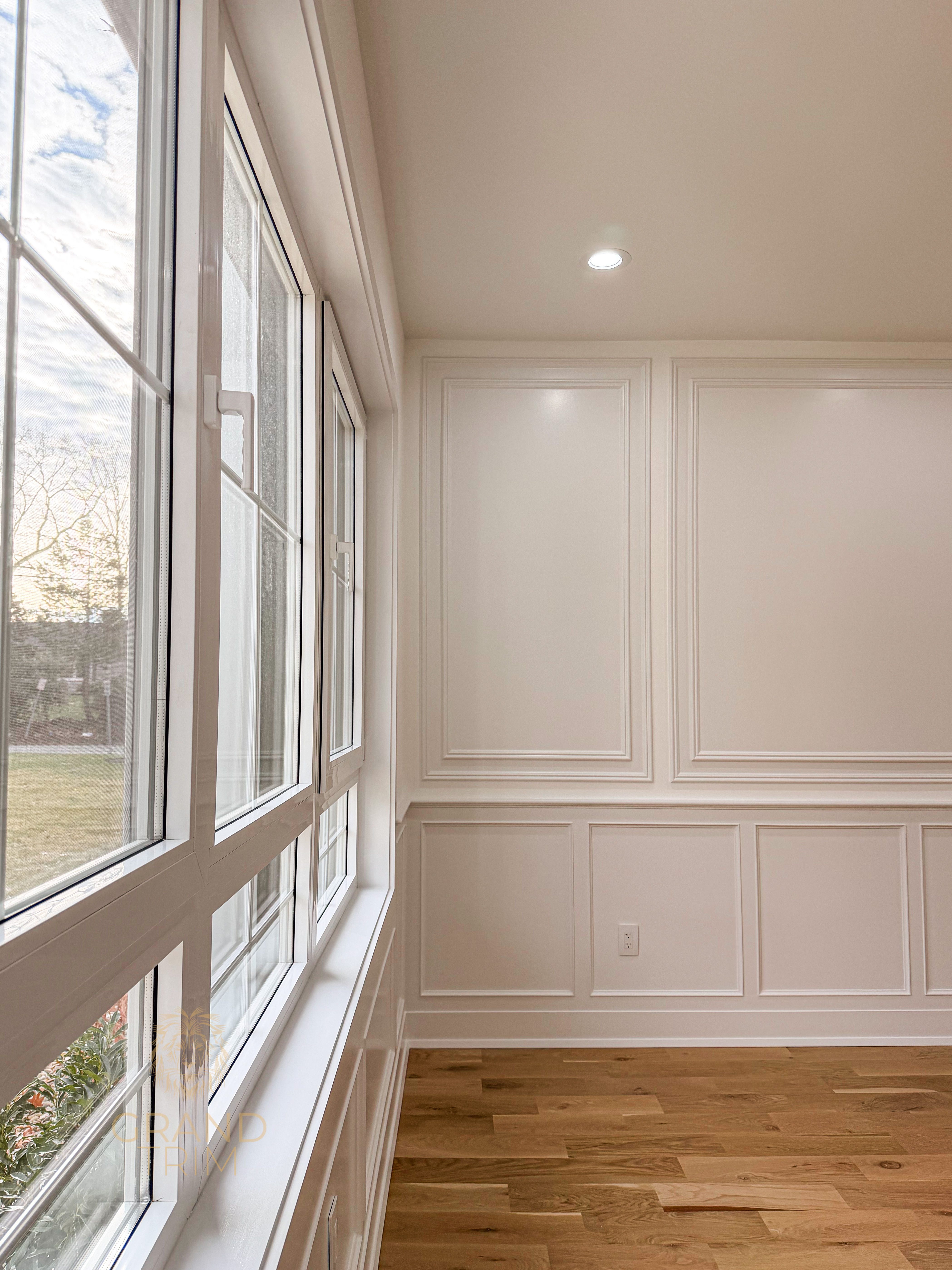 White wall paneling with decorative picture frame molding in a New Jersey room with large windows
