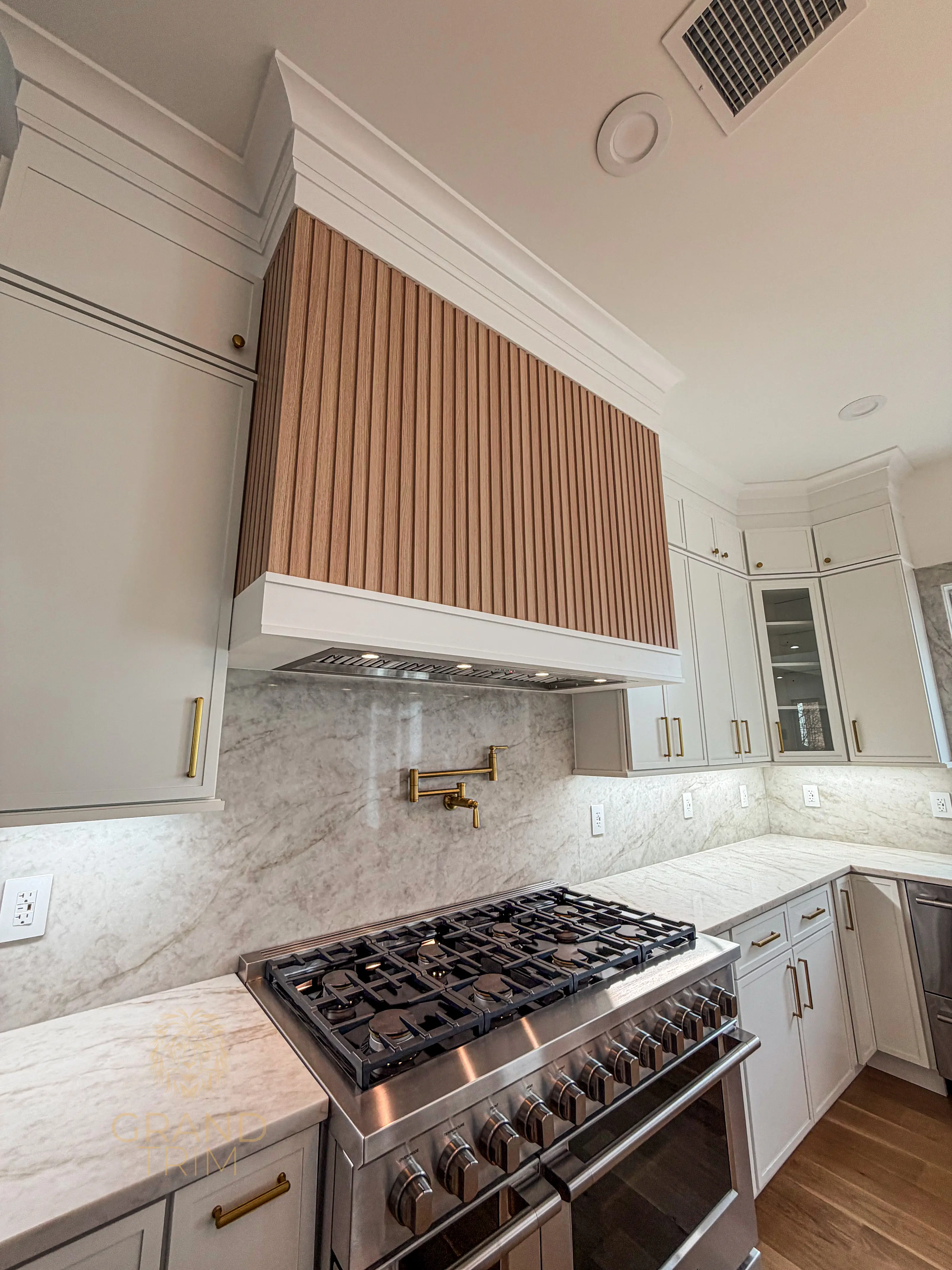 Custom white kitchen cabinetry with a wood slatted range hood and intricate crown molding in a New Jersey home.