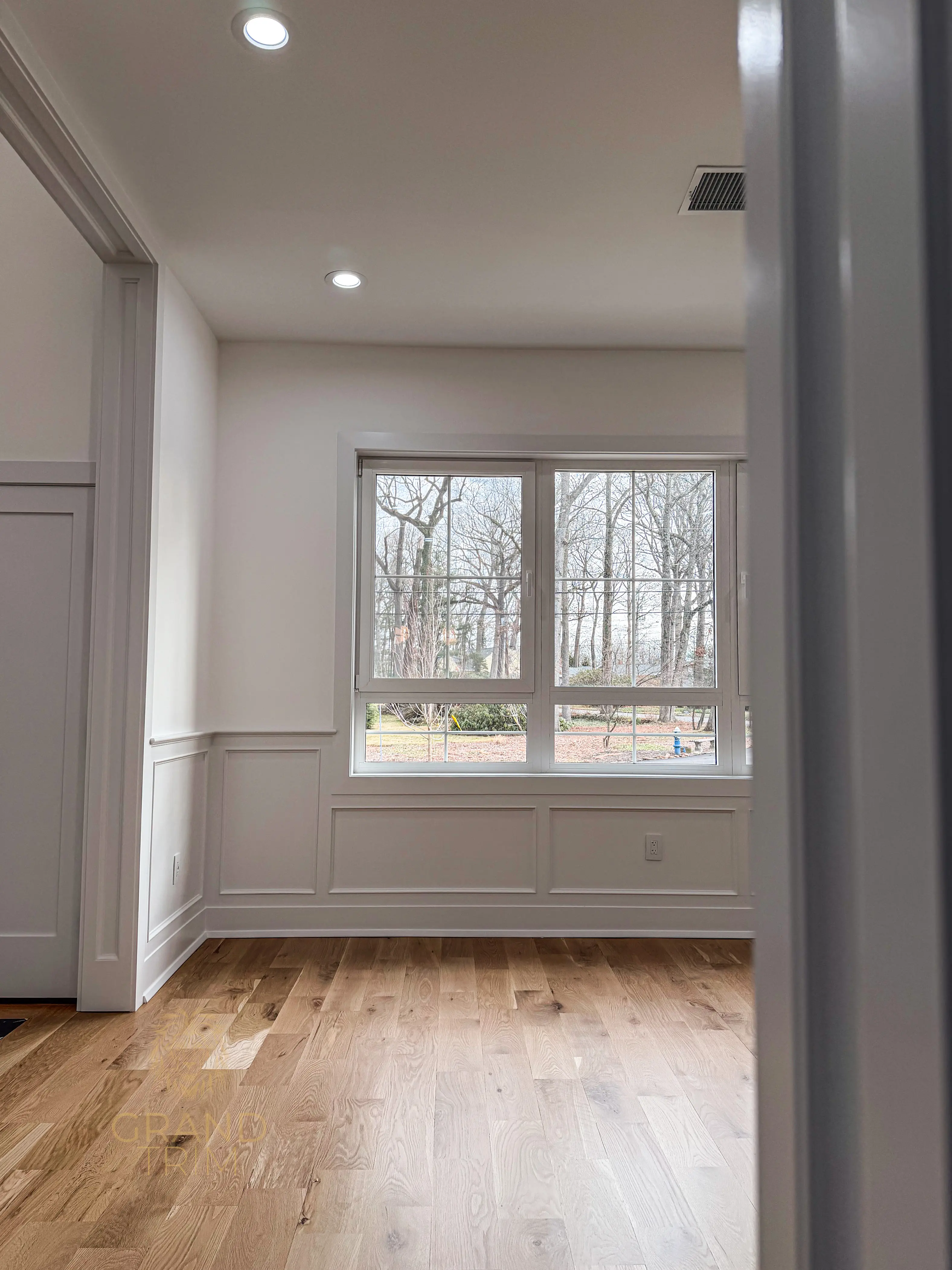 White wainscoting with decorative panels, window casing, and doorway trim in an empty New Jersey room