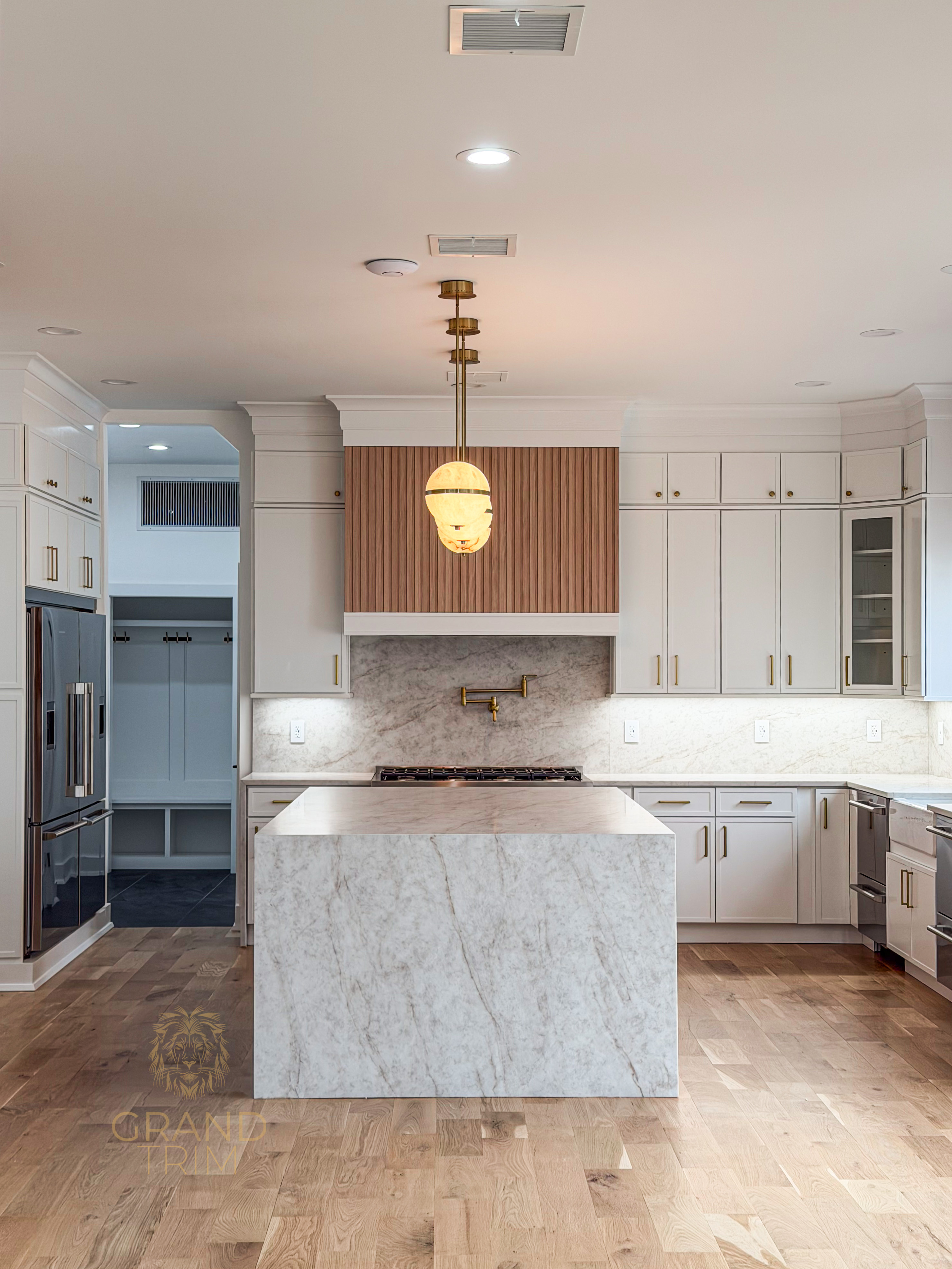 Modern white kitchen with custom cabinetry, marble island, wood fluted range hood, and mudroom entryway in background in NJ