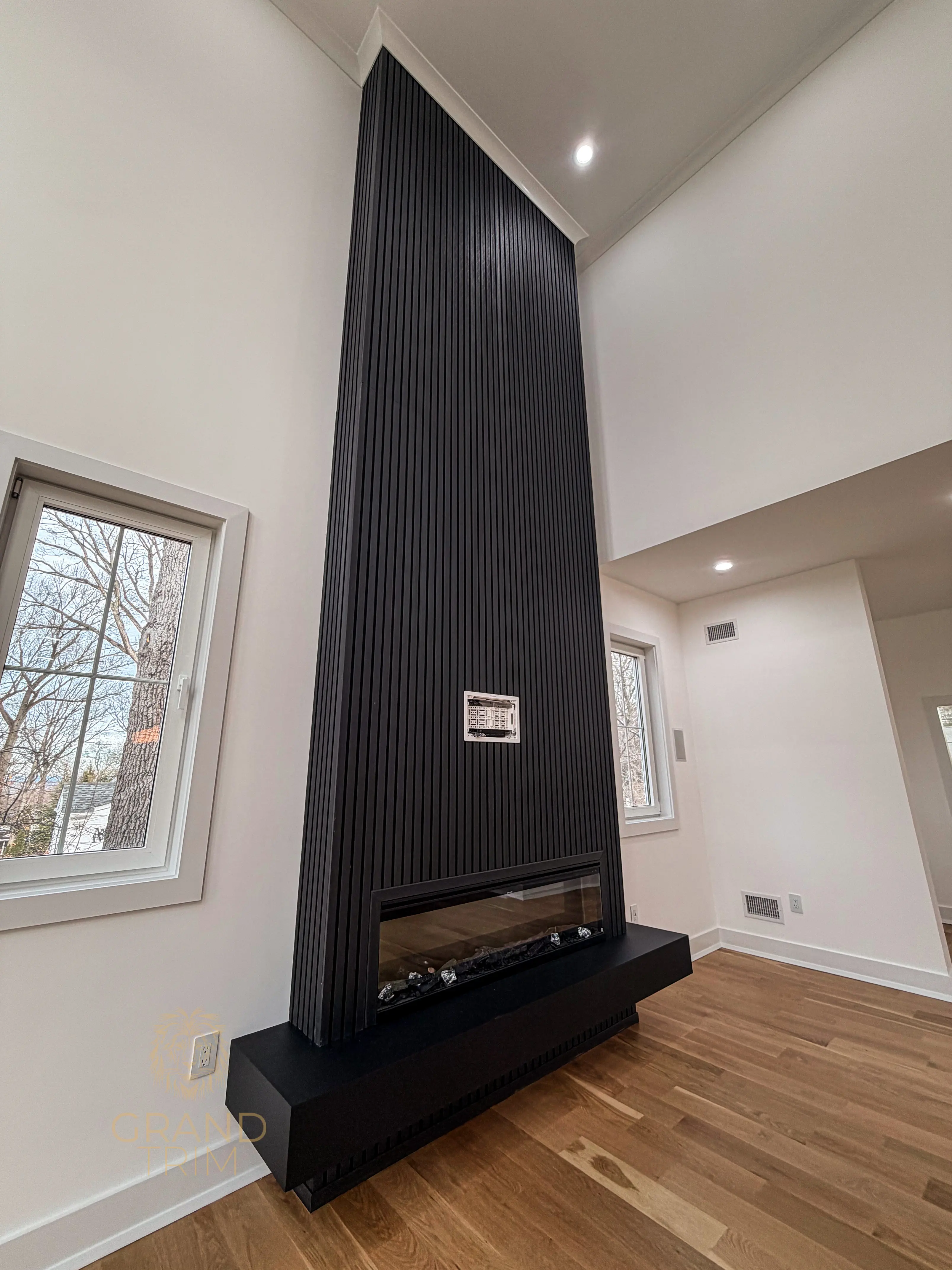 Modern black slatted wall paneling encompassing a linear electric fireplace in a high-ceiling New Jersey living room