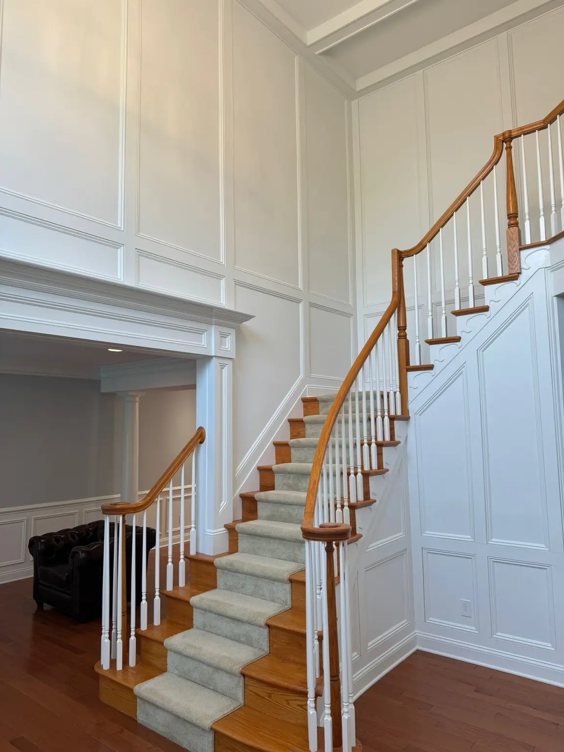 White full-height wall paneling and a tray ceiling in a grand New Jersey entryway with a curved staircase