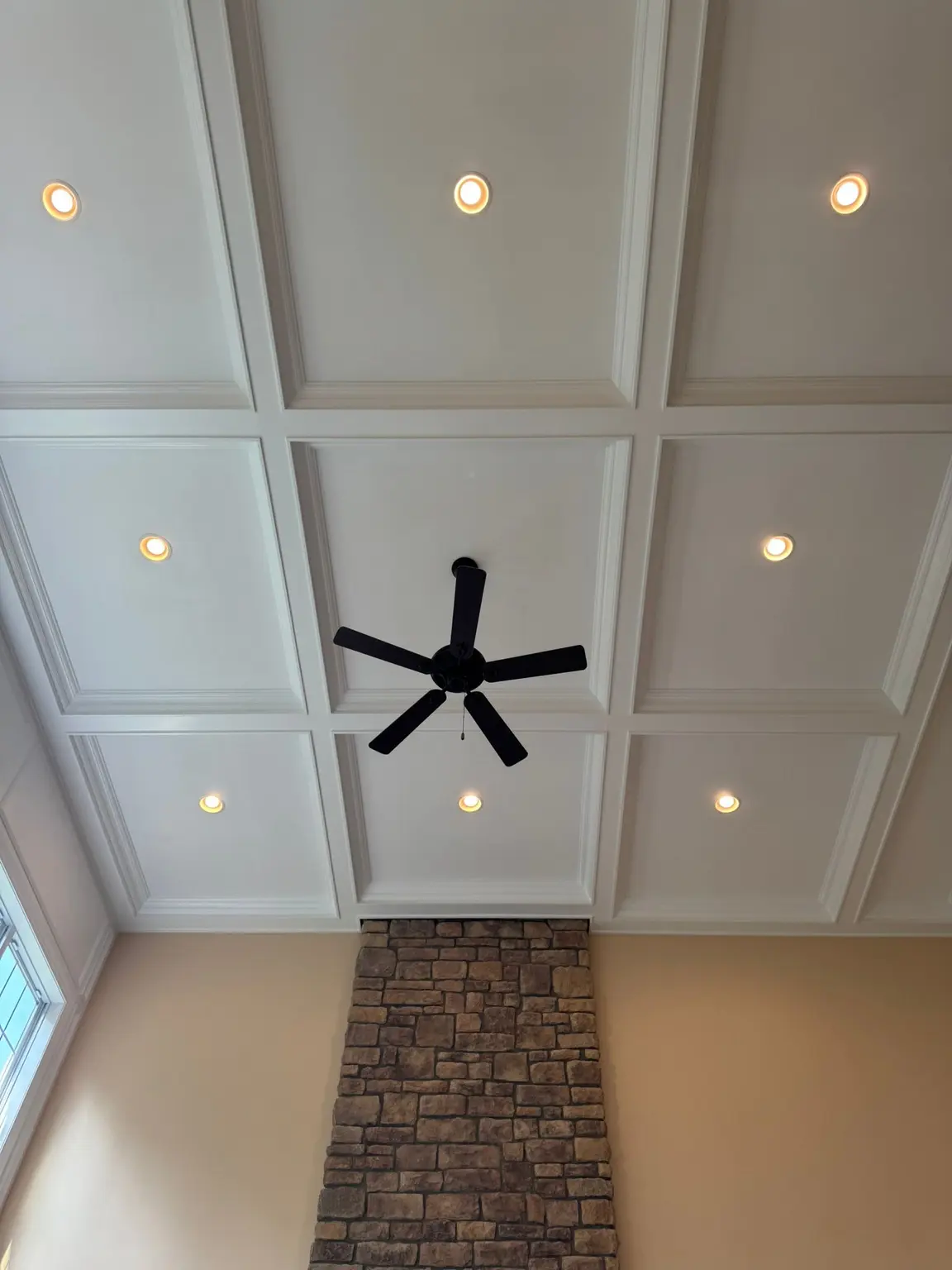 White coffered ceiling with square recessed panels, integrated lighting, and a black fan above a stone chimney in a New Jersey living space