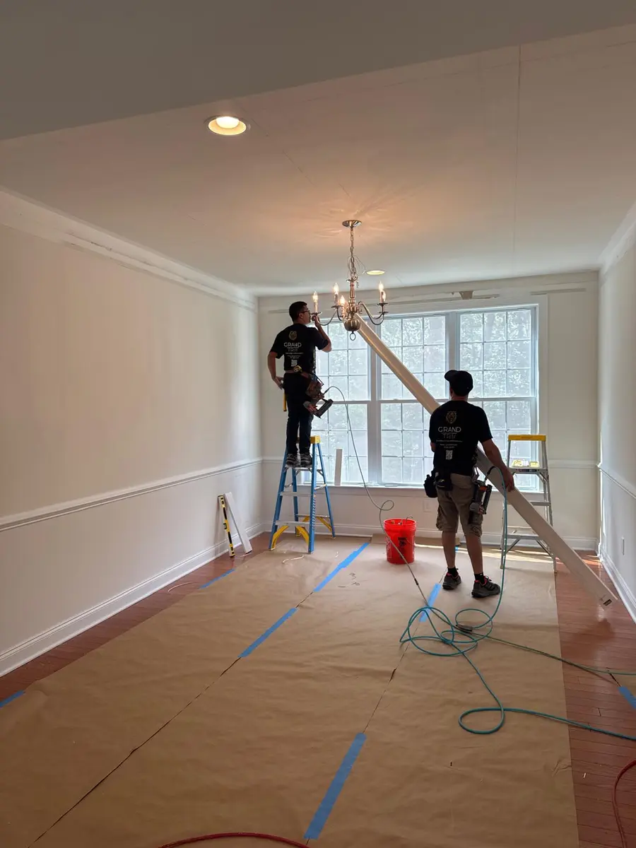 Workers installing white crown molding and chair rail trim in a New Jersey room