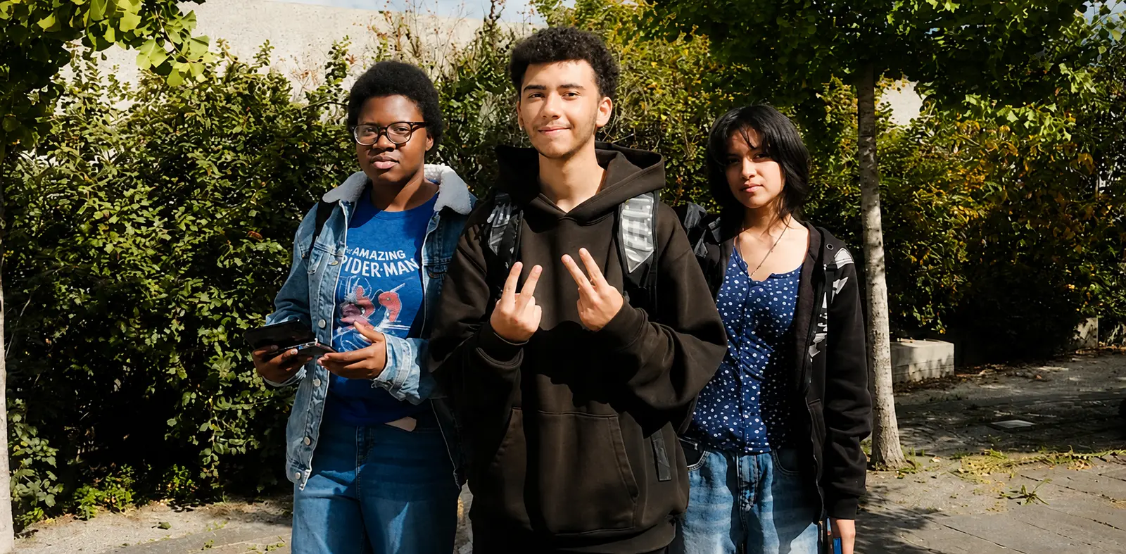 Three students with backpacks walking outside on a sunny day