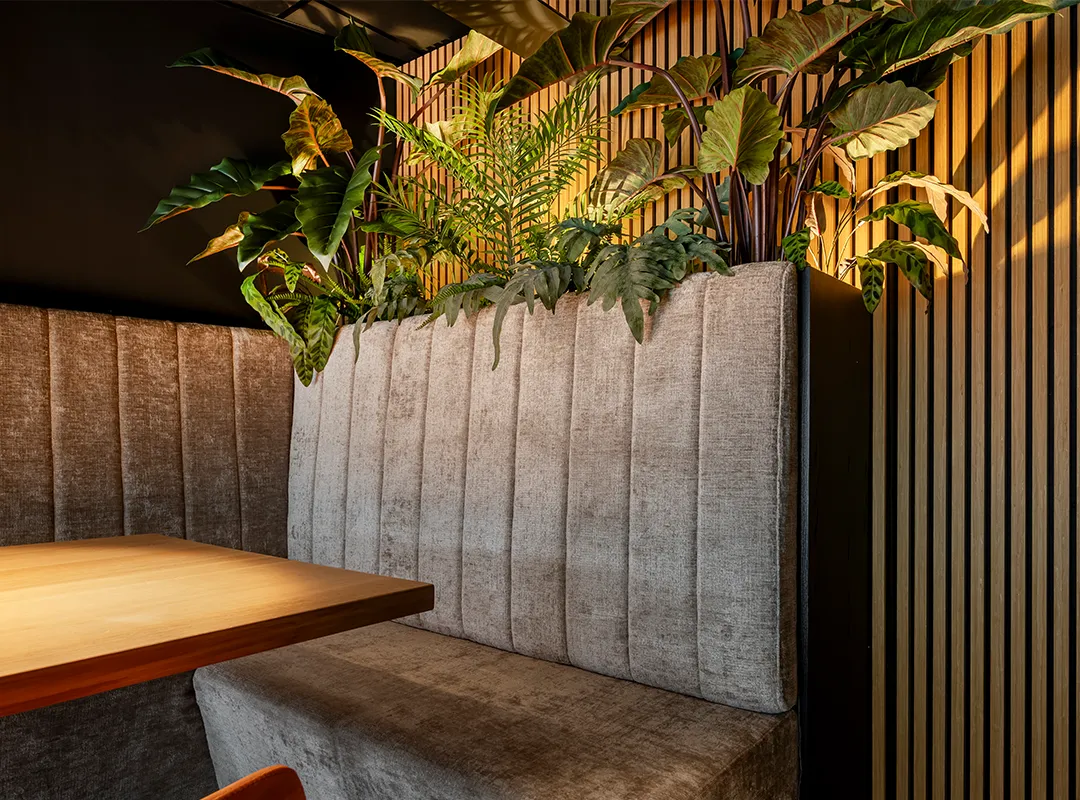 Interieurbeplanting verwerkt in een stijlvolle zithoek met grijze bank en houten lambrisering