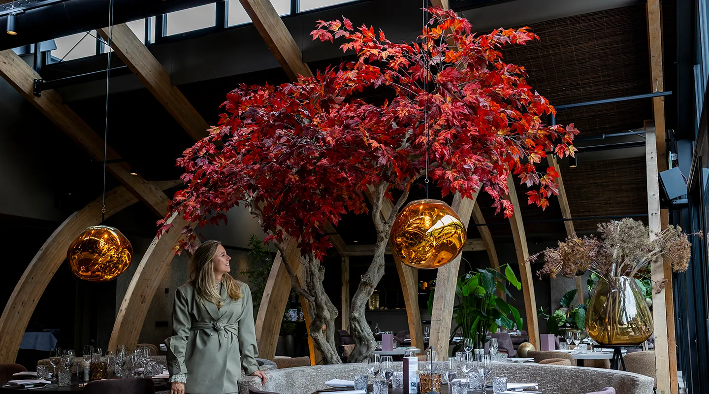 Oprichter Michelle Peterman van Miverde bewondert de maatwerk rode boom in een stijlvol restaurant