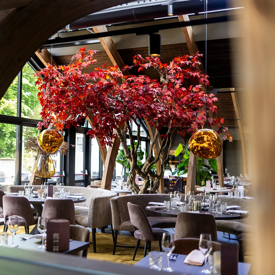 Twee grote rode maatwerk bomen als indrukwekkende groene installatie in een luxe restaurantzaal