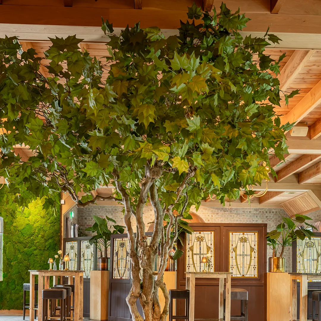 Maatwerk kunstboom met groene bladeren als sfeerbepalende eyecatcher midden in een horecainterieur
