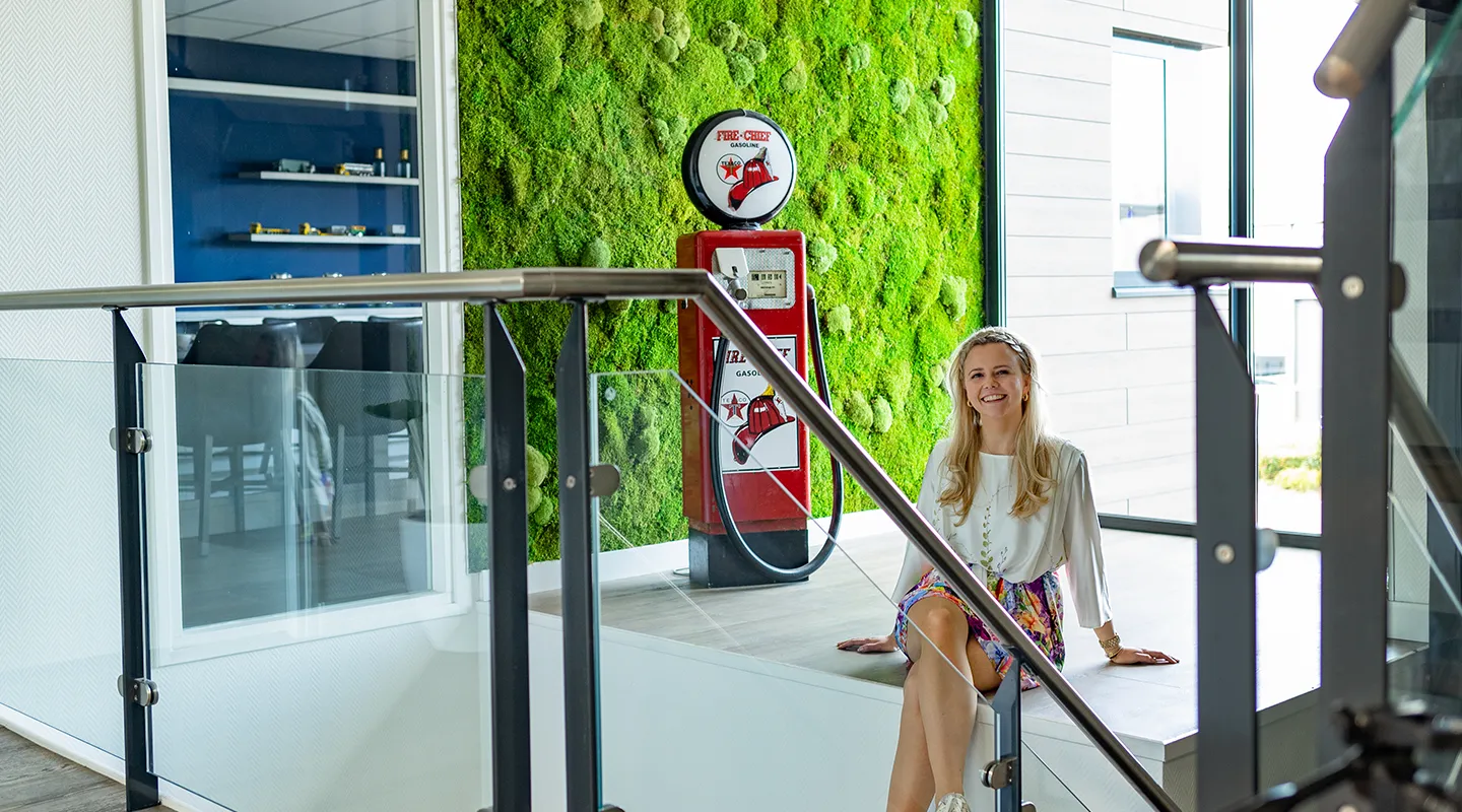 Michelle Peterman van MiVerde zit voor een grote bolmos moswand naast een vintage benzinepomp in een kantoor