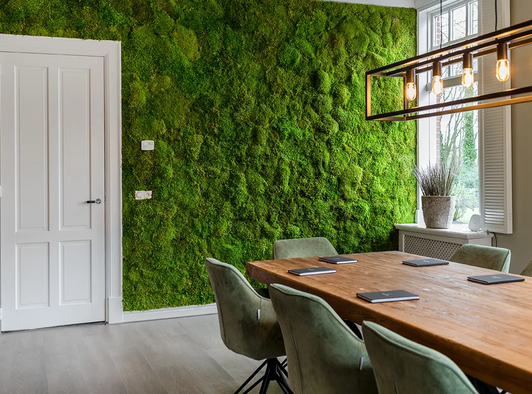 Volledige groene bolmos moswand van vloer tot plafond in een lichte vergaderruimte met houten tafel