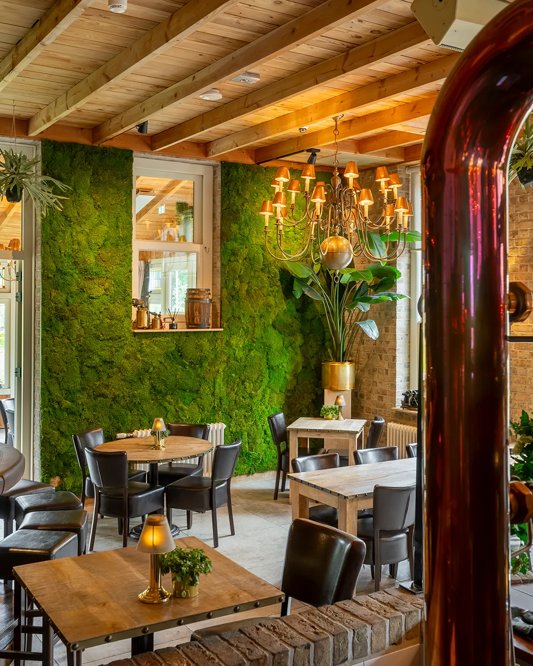 Restaurant met verticale groene moswand, houten plafondbalken, warme verlichting en natuurlijke inrichting