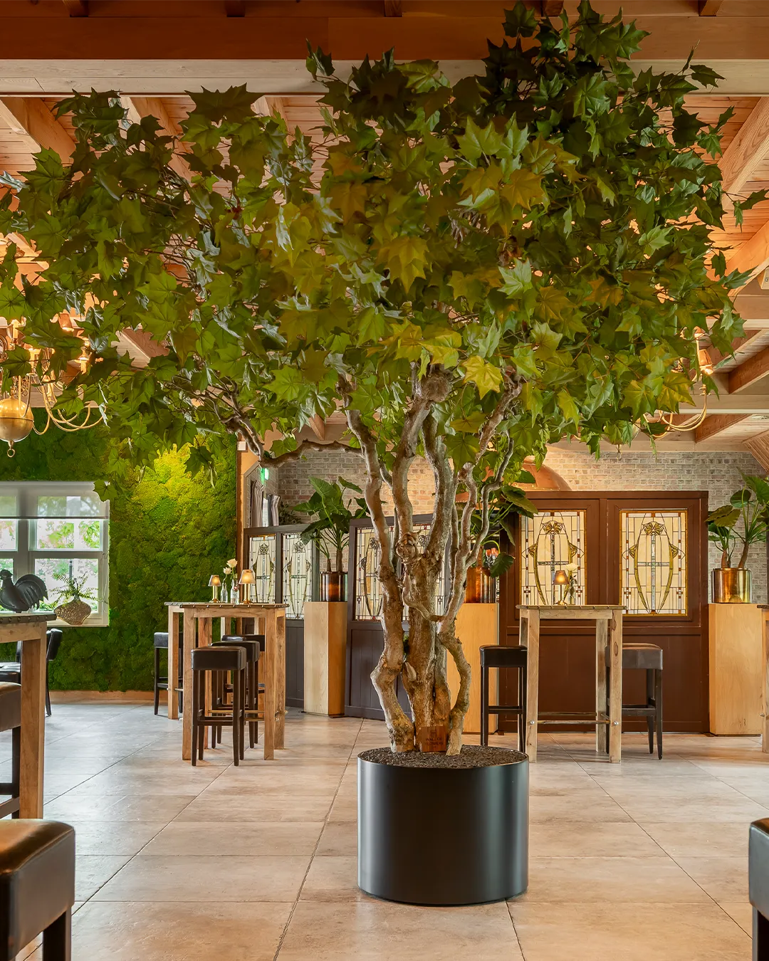 Grote decoratieve boom met groene bladeren als centraal element in modern restaurant interieur met houten accenten