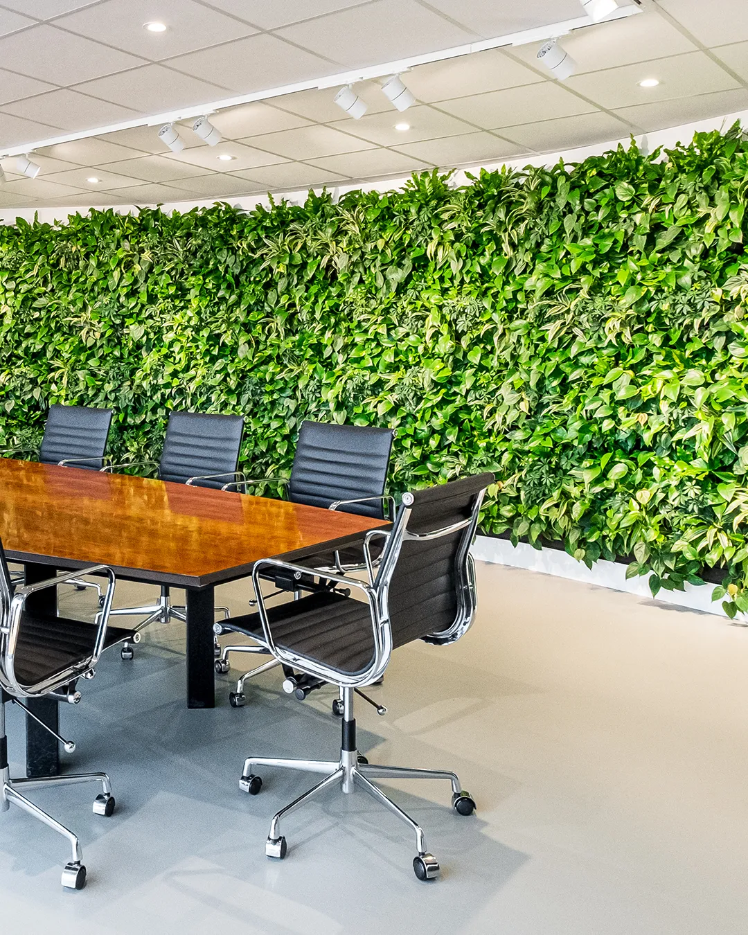 Verticale plantenwand in vergaderzaal met houten tafel en designstoelen voor duurzaam kantoorinterieur