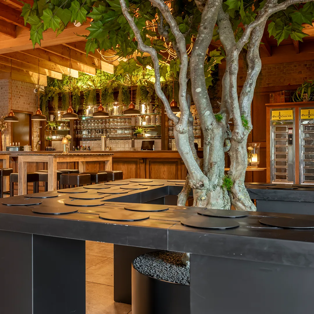 Sfeervol restaurant interieur met grote boom, houten bar, koperen lampen en moderne inrichting