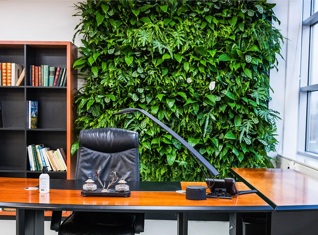 Modern kantoor met verticale groene plantenwand achter bureau met zwarte stoel en houten tafel