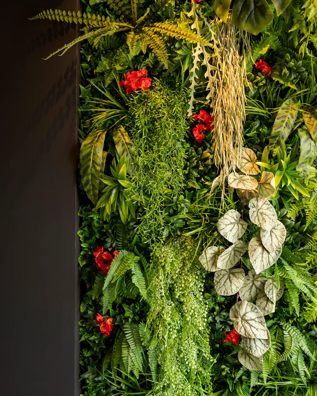Verticale plantenwand met varens, rode bloemen en tropische bladeren als groene wanddecoratie