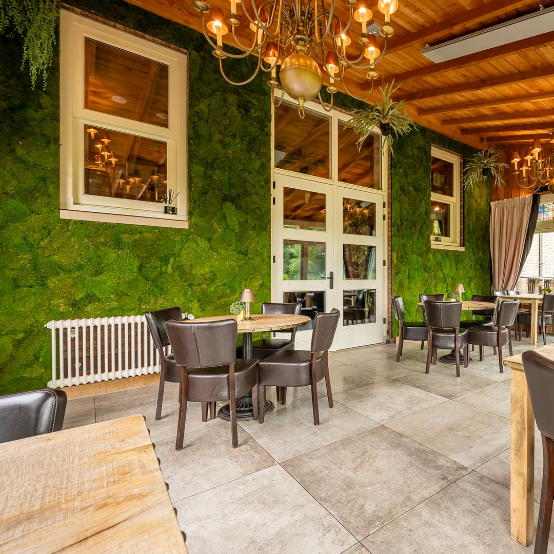 Restaurant met groene verticale moswand, houten plafondbalken, vintage kroonluchters en ronde tafels