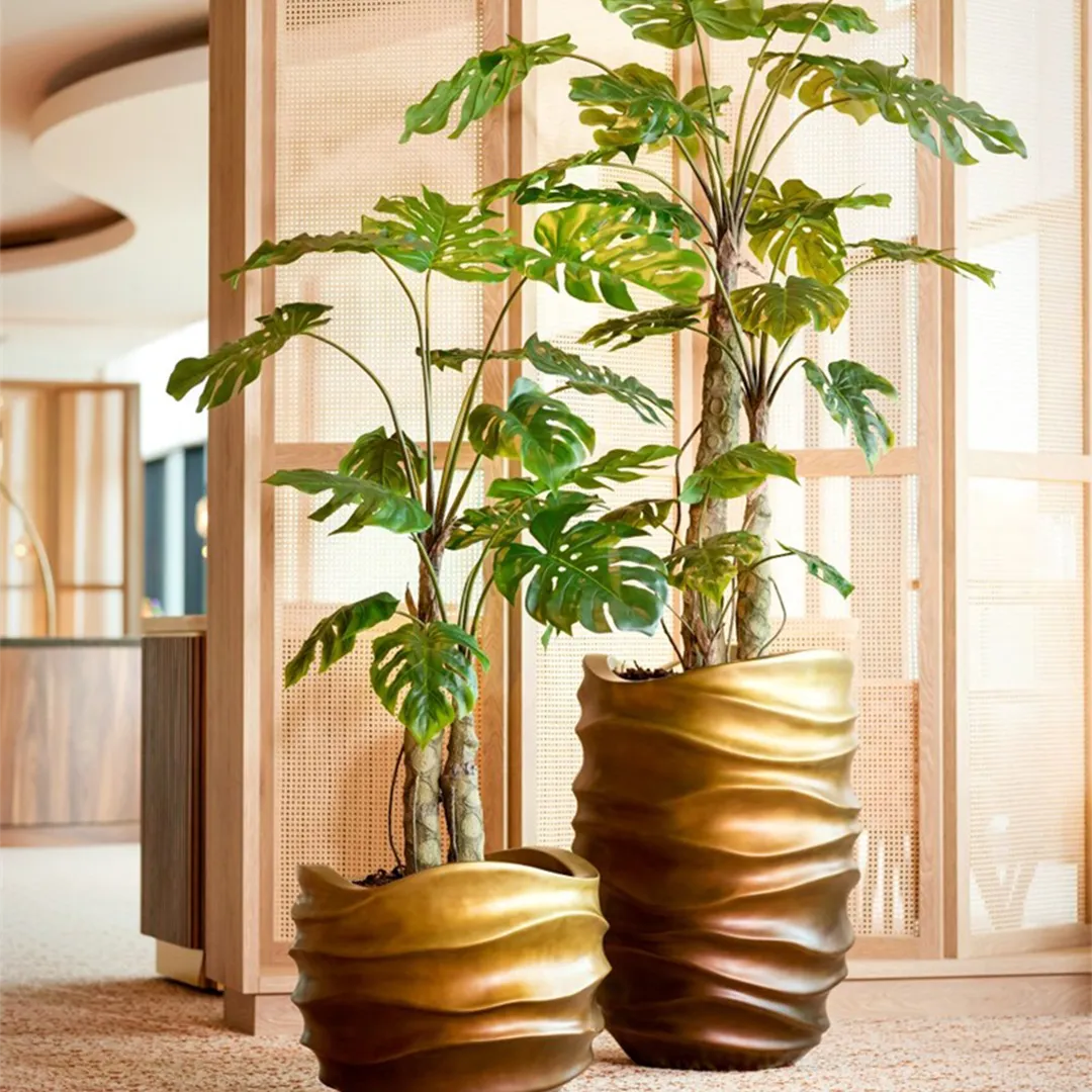 Gouden organische plantenpotten met Monstera planten tegen rotan kamerscherm in modern interieur