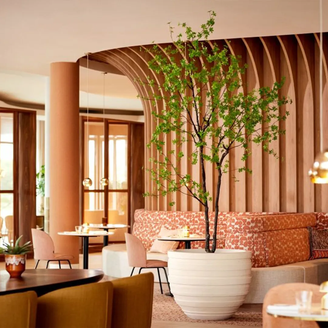 Warm restaurant interieur met organische houten wand, decoratieve boom en roze banken in eigentijdse stijl