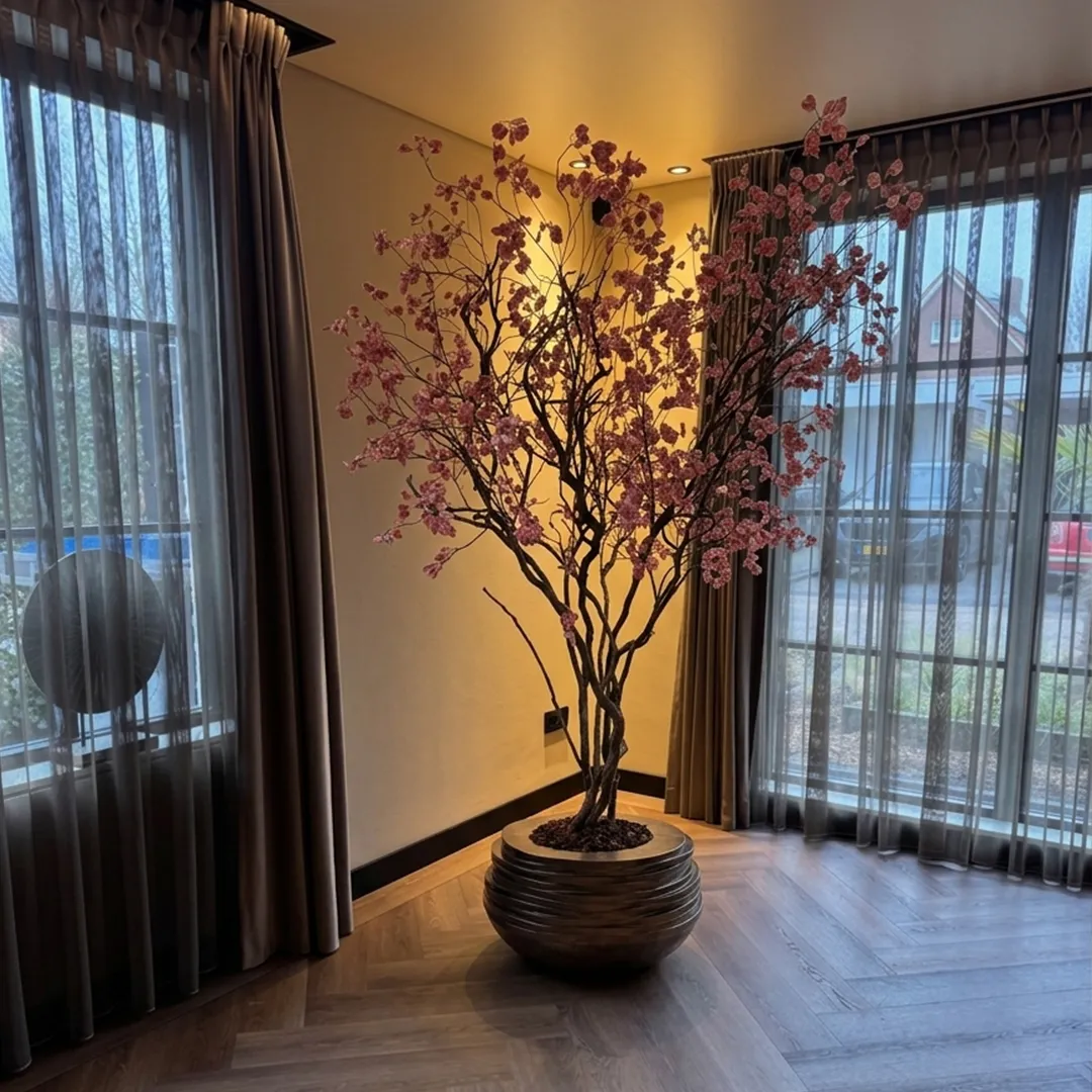 Elegante roze kersenbloesem arrangement in zwarte vaas bij grote ramen met sheer gordijnen in modern interieur
