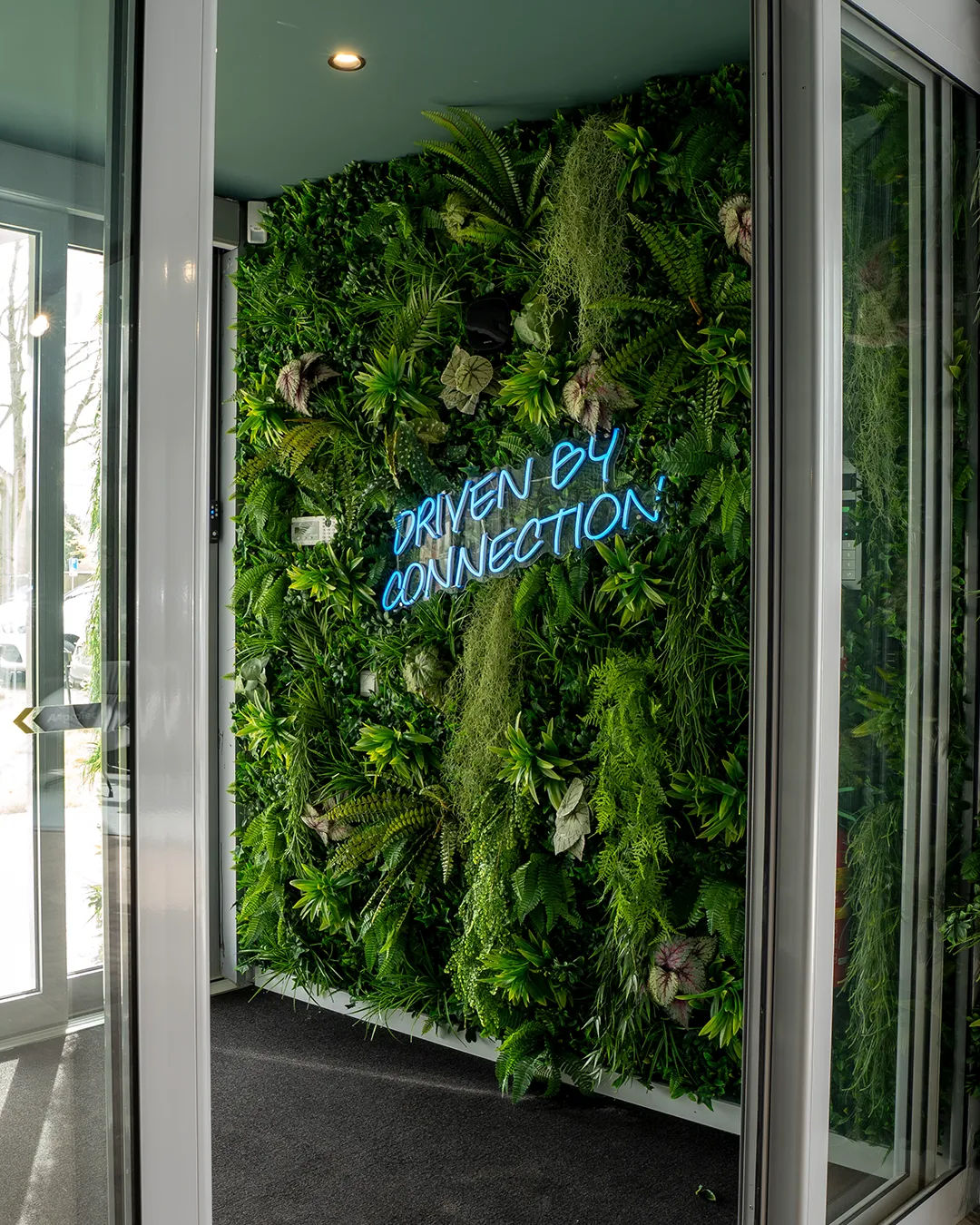 Verticale groene plantenwand met neonlicht met de tekst 'Driven by Connection' in een moderne kantoorentree — gerealiseerd door Miverde