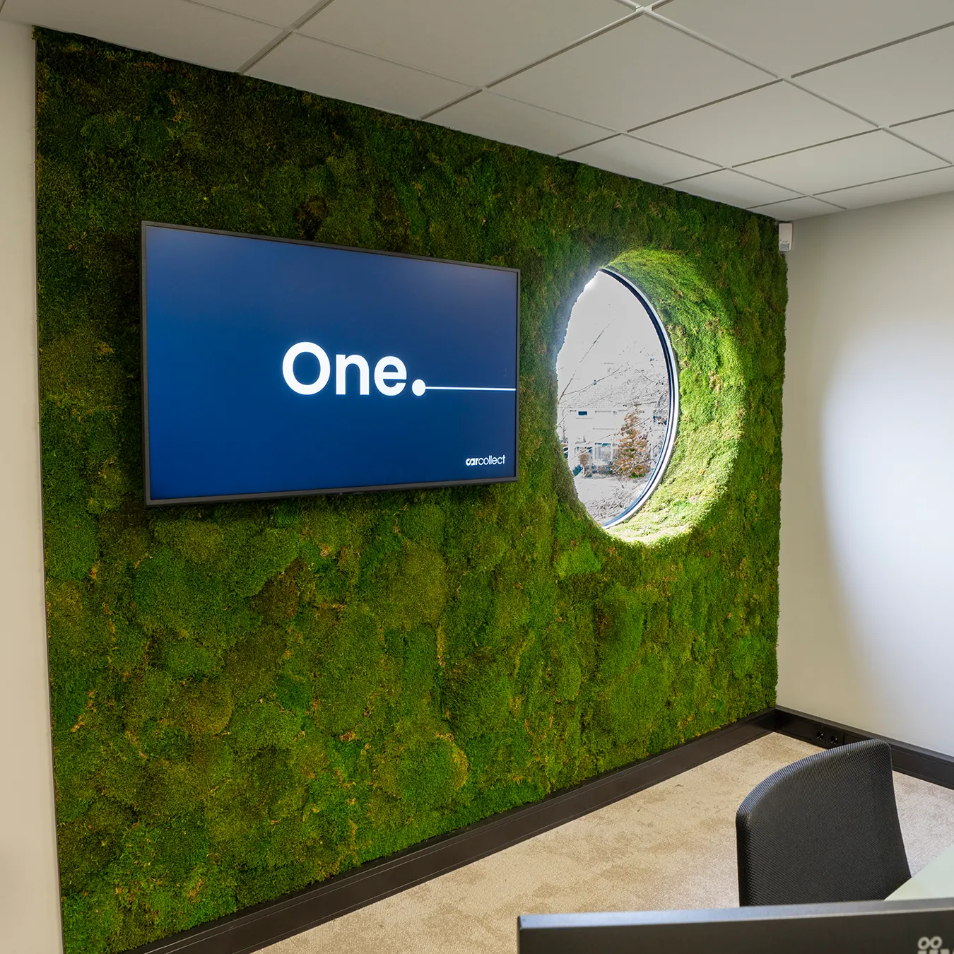 Groene mosswand met ingebouwde flatscreen tv en rond raamuitsparing in een moderne kantoorvergaderruimte — maatwerk groene wanddecoratie door Miverde