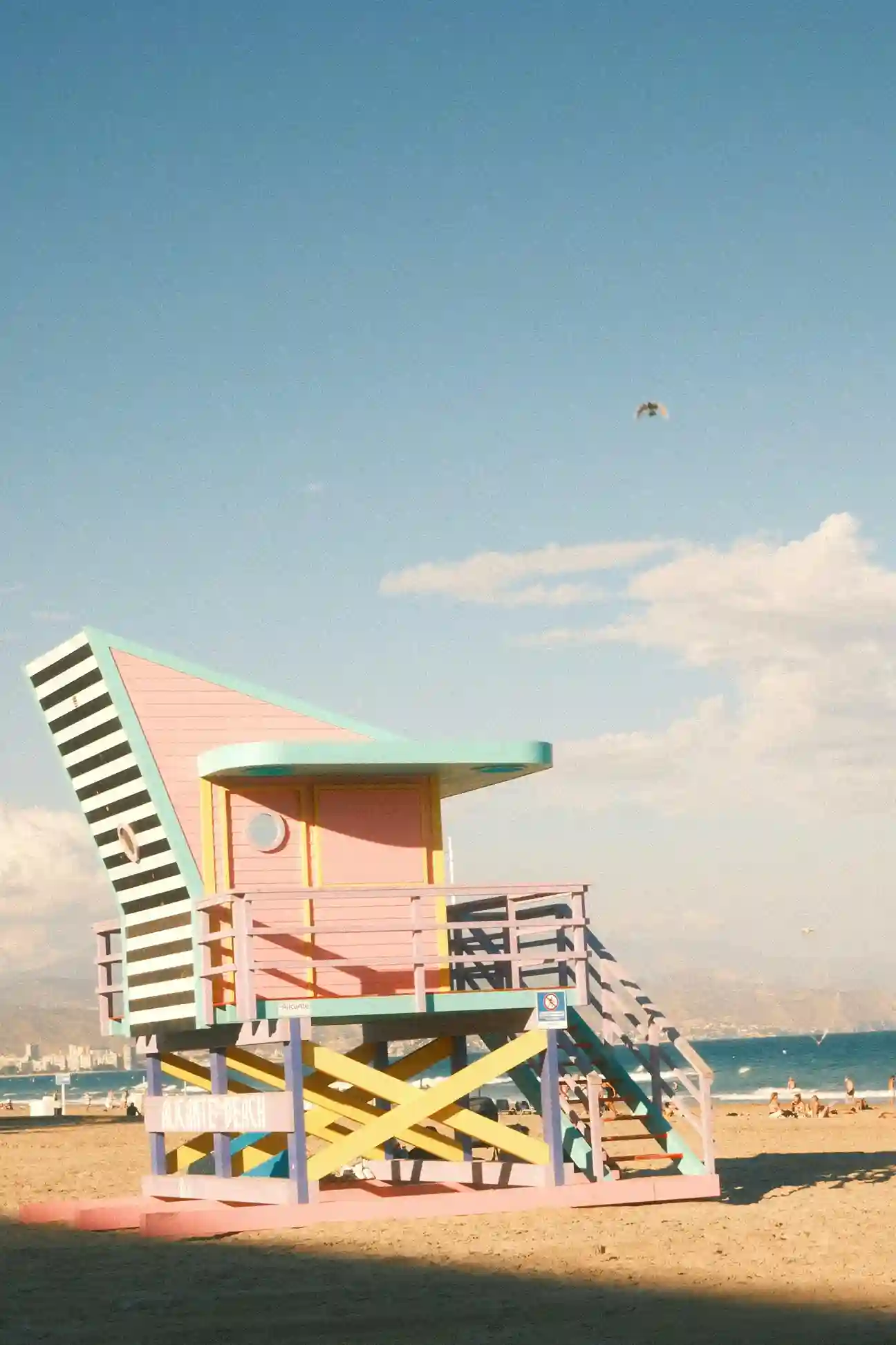 Colorful lifeguard tower on a sandy beach with ocean and distant mountains under a blue sky.