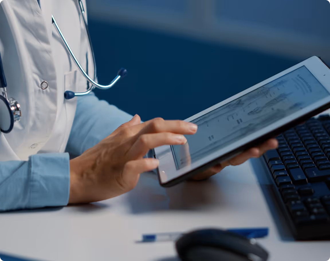 Medical professional using a tablet displaying a digital anatomy chart next to a computer keyboard.