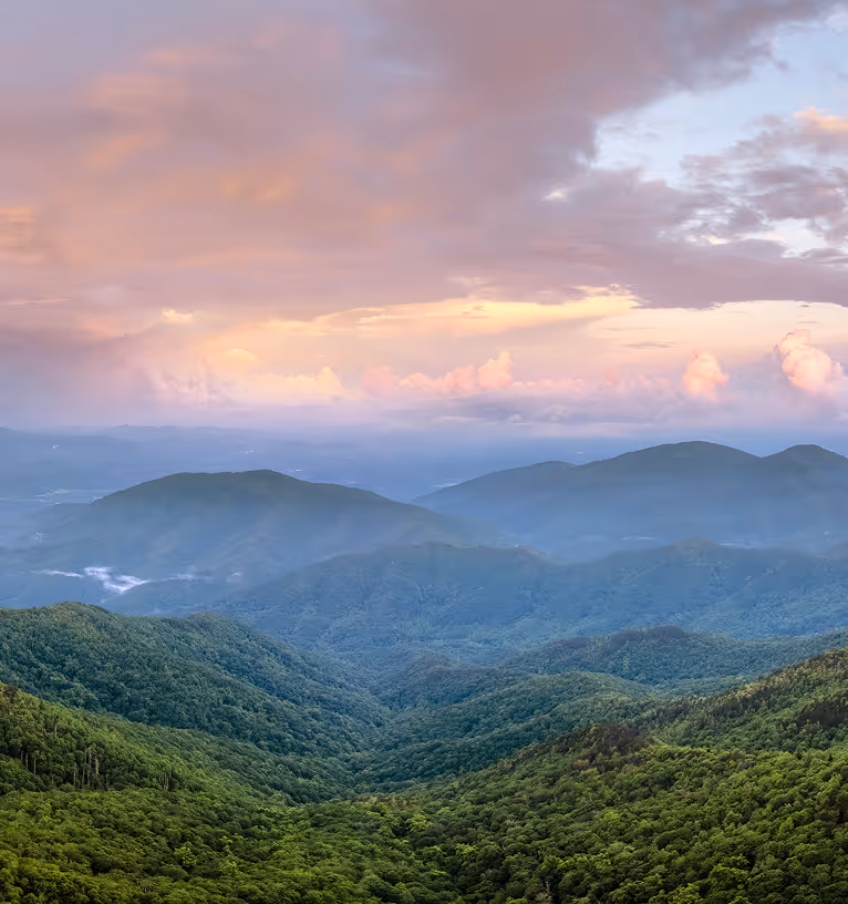 Lush green mountains under a cloudy sky during sunset with soft pink and orange hues.