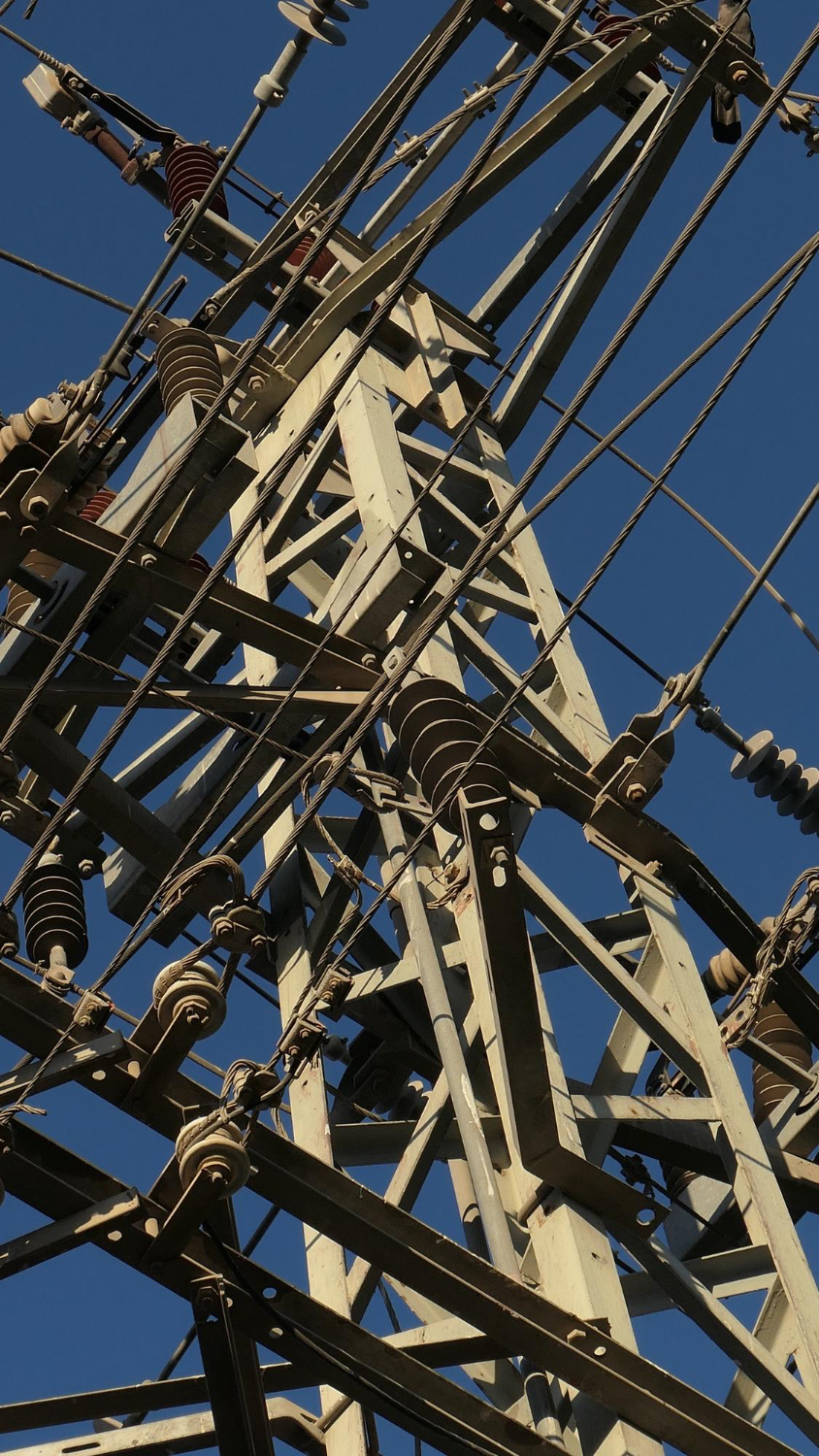 Close-up view of metal electrical substation structure with multiple insulators and power lines against a clear blue sky.