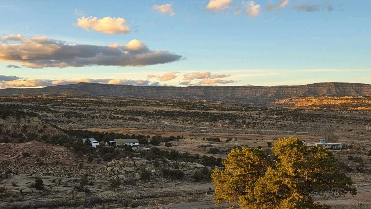 Scenic view of Coyote Hills North, Utah, showcasing vast open land, distant mountains, and a few structures, emphasizing off-grid living and recreational opportunities for potential land buyers.