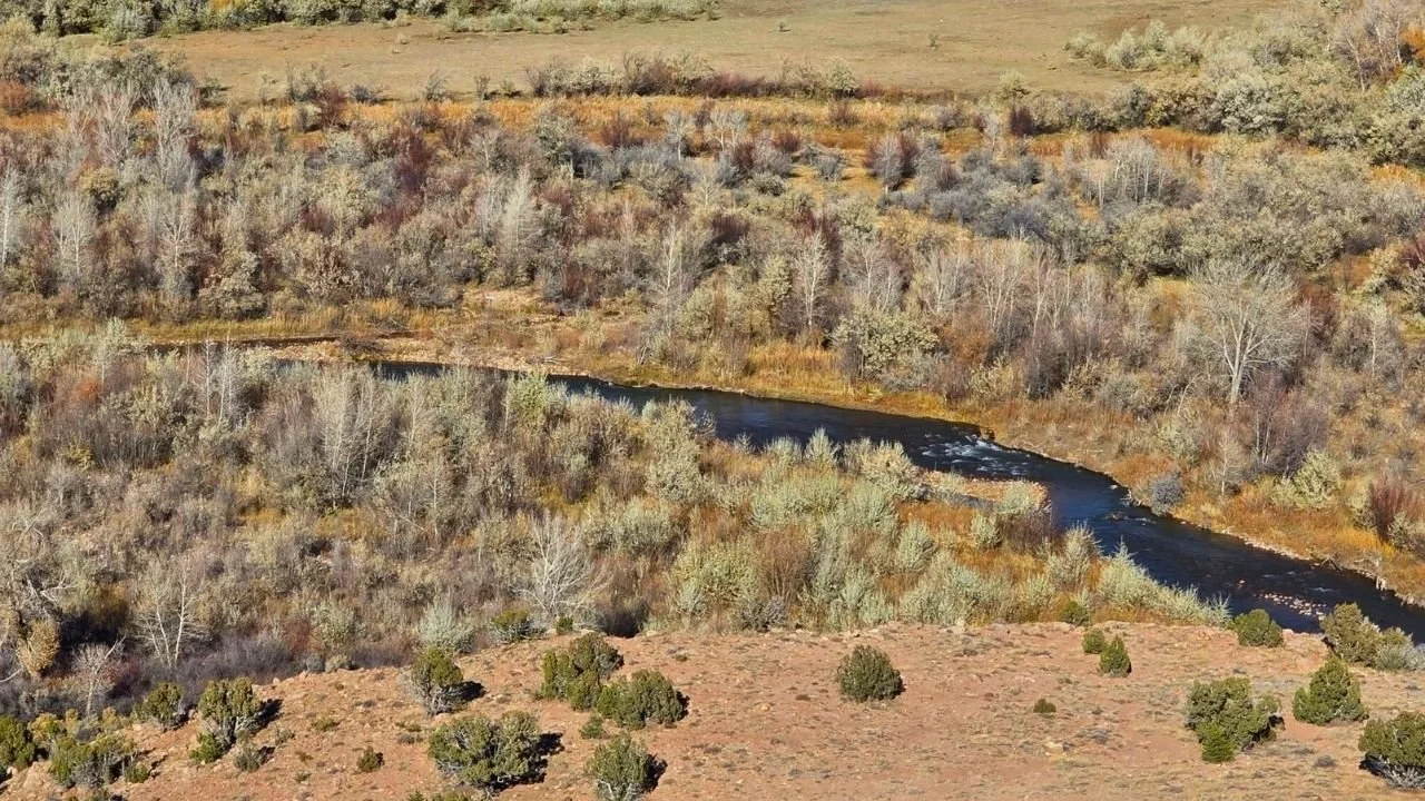 Aerial view of a 4.97-acre lot in Conejo Hills, Utah, featuring a winding river, diverse vegetation, and open land, ideal for residential or recreational development.
