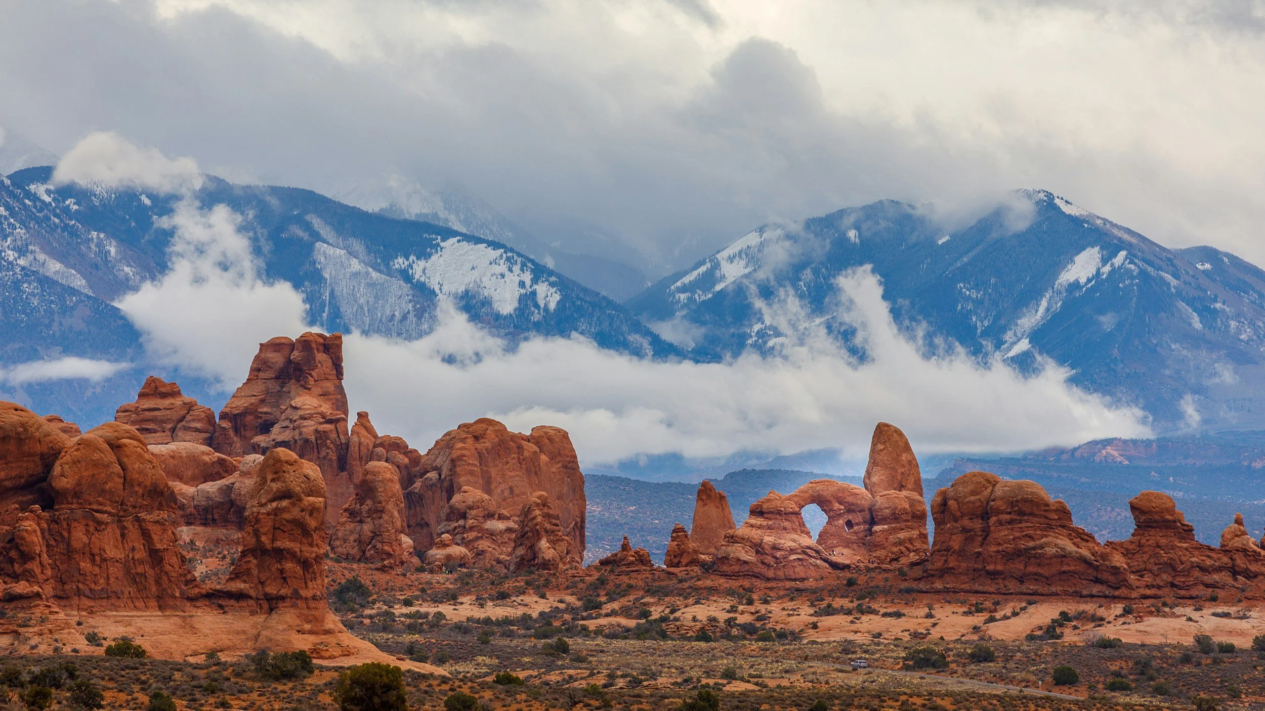 Red rock formations and natural arches under a cloudy sky in Arches National Park, Utah, showcasing the region's stunning landscapes and outdoor adventure opportunities.