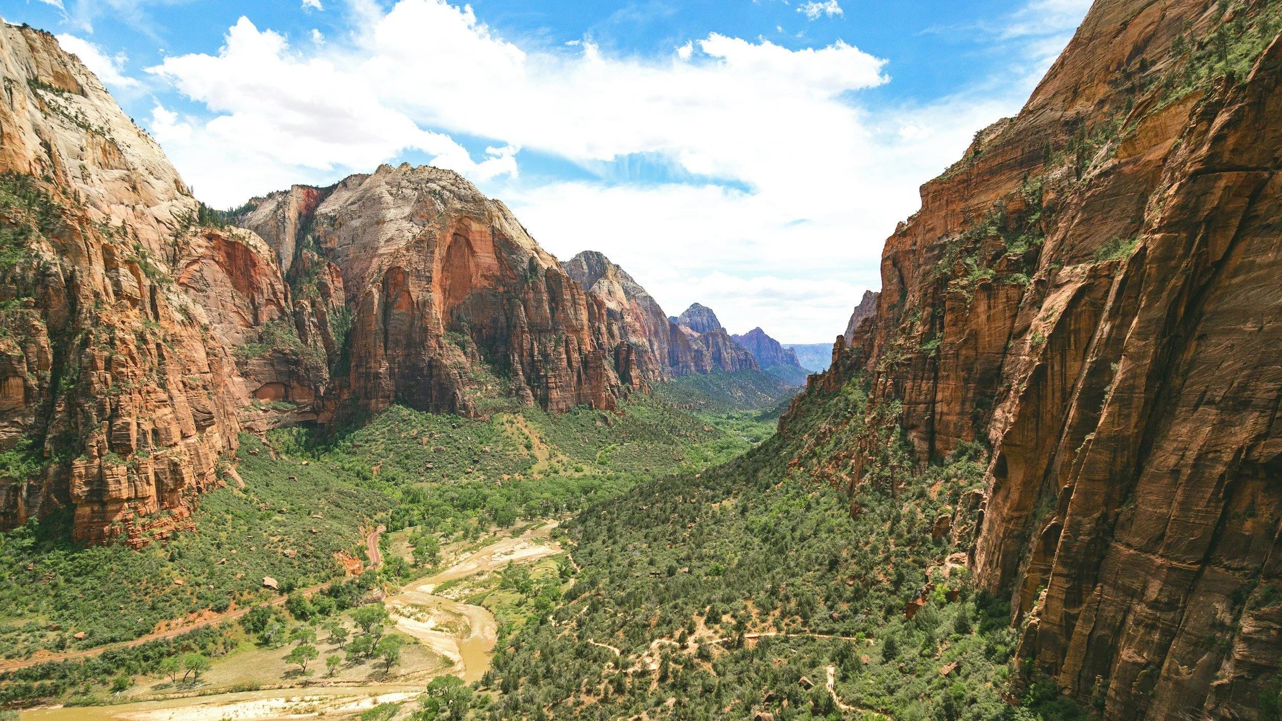 Zion National Park landscape featuring towering red rock cliffs, lush green valley, and blue sky, highlighting Utah's natural beauty and outdoor adventure opportunities.