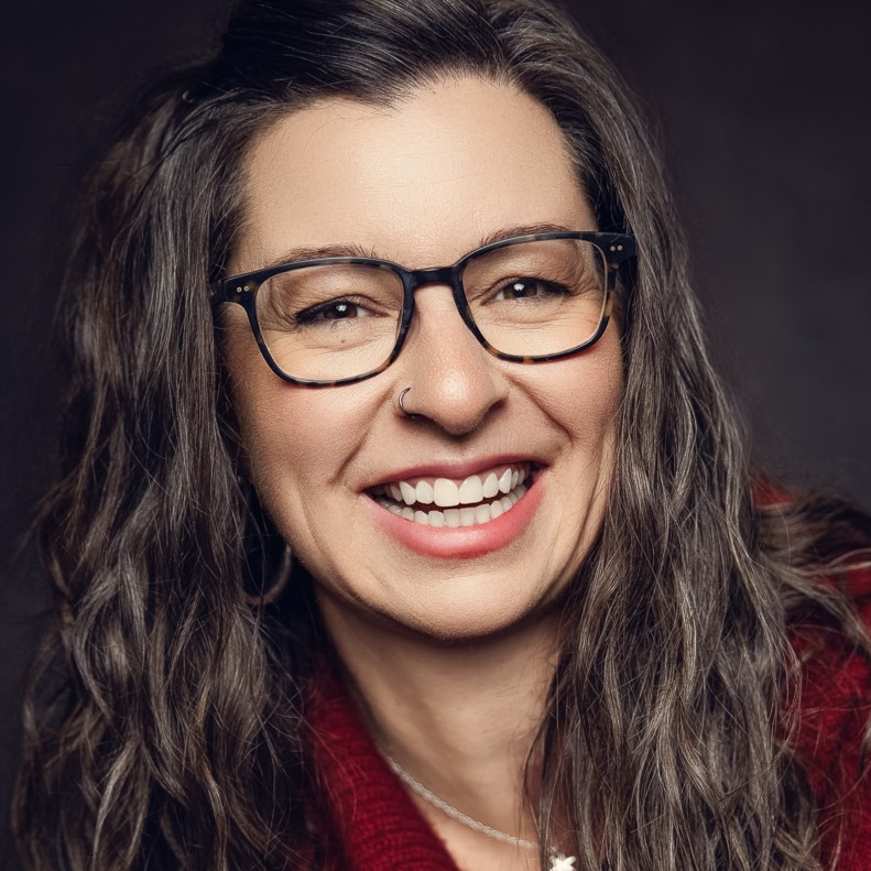 Smiling woman with long wavy hair and black glasses wearing a red sweater.