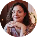 Smiling woman with curly hair resting her chin on her folded hands, wearing a floral patterned top.