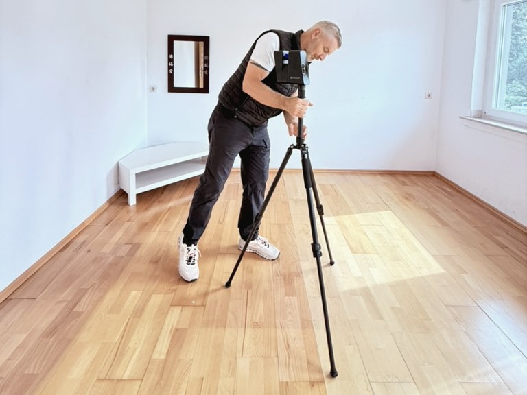 René Schulte beim Aufmaß mit Messstativ in einem leeren Raum